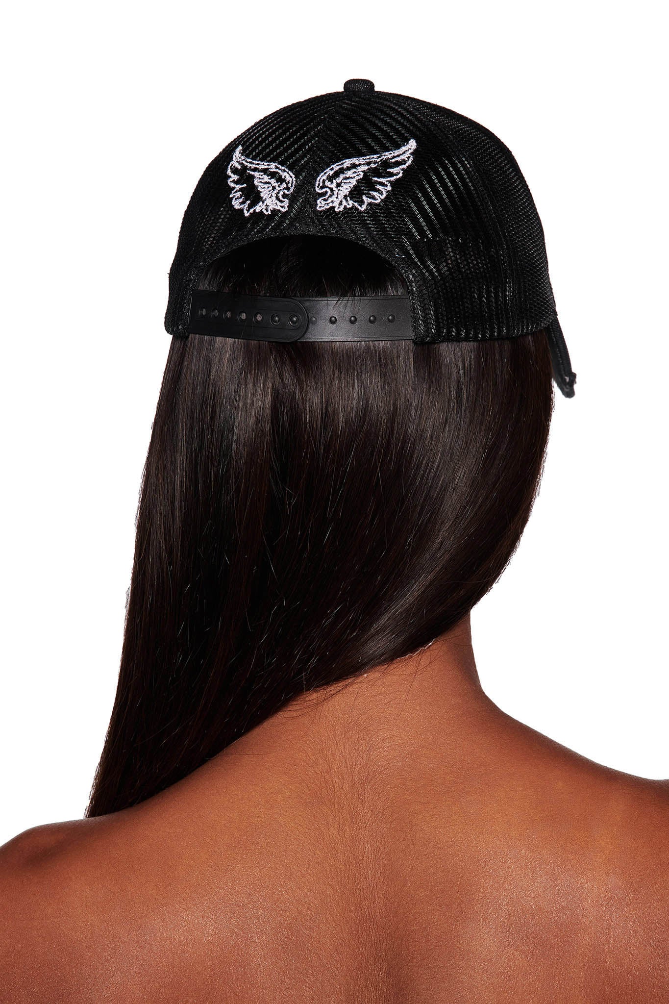 A person with long, dark hair is seen from behind, wearing a black I.AM.GIA KIMANI CAP featuring embroidered white wings on the back. The person's shoulders are bare and the adjustable strap of the cap is visible.