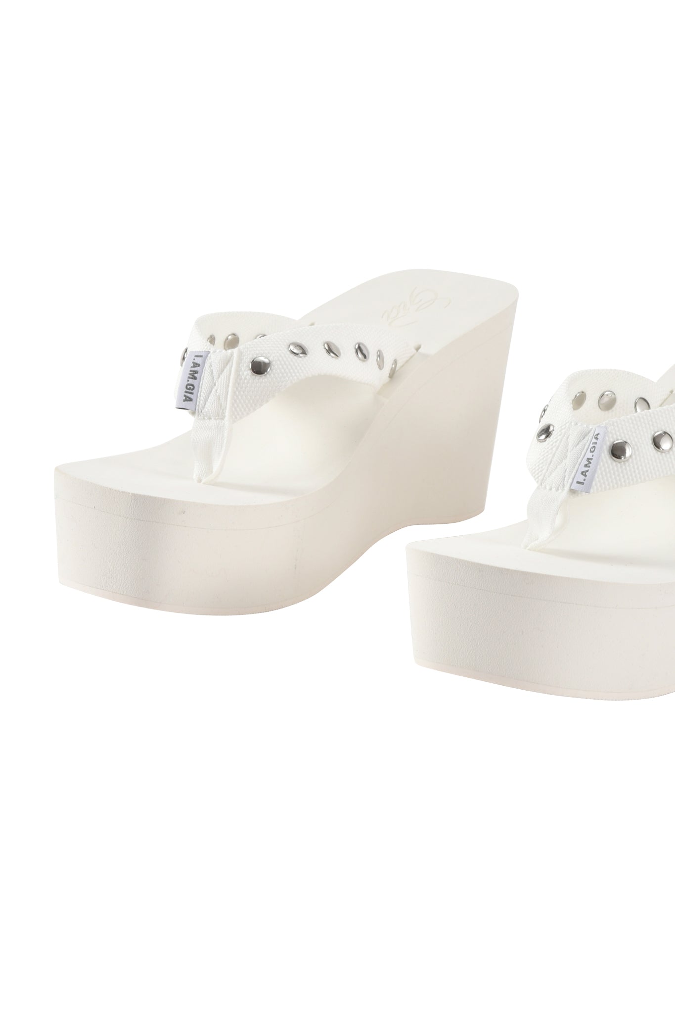 The I.AM.GIA SHELBY STUDDED FLIP FLOP 2.0 in white features wedge platforms, mesh straps, and silver studs, displayed on a plain white background.