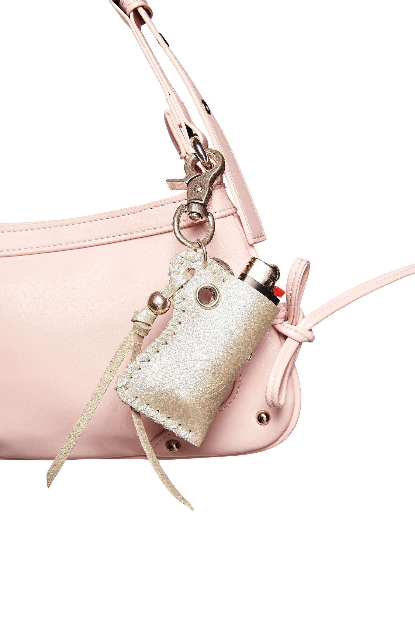 Close-up of a light pink leather handbag with the I.AM.GIA VENUS LIGHTER KEYCHAIN - SILVER in beige attached to the strap by a metal clasp, featuring stitched edges, a small leather tie, and an embossed GIA logo.