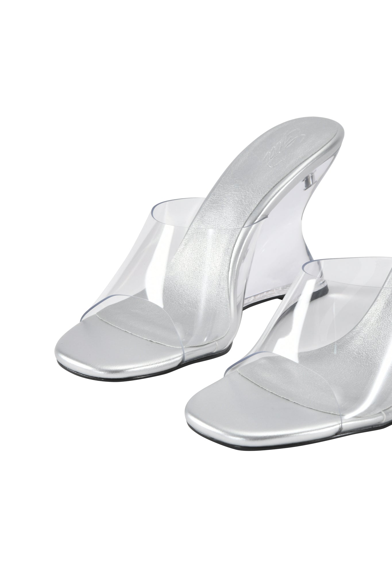 The I.AM.GIA RHEA CLEAR WEDGE HEEL - TRANSPARENT features open-toe, slip-on sandals with clear vinyl straps, metallic silver footbeds, and a transparent wedge heel, shown against a white background.