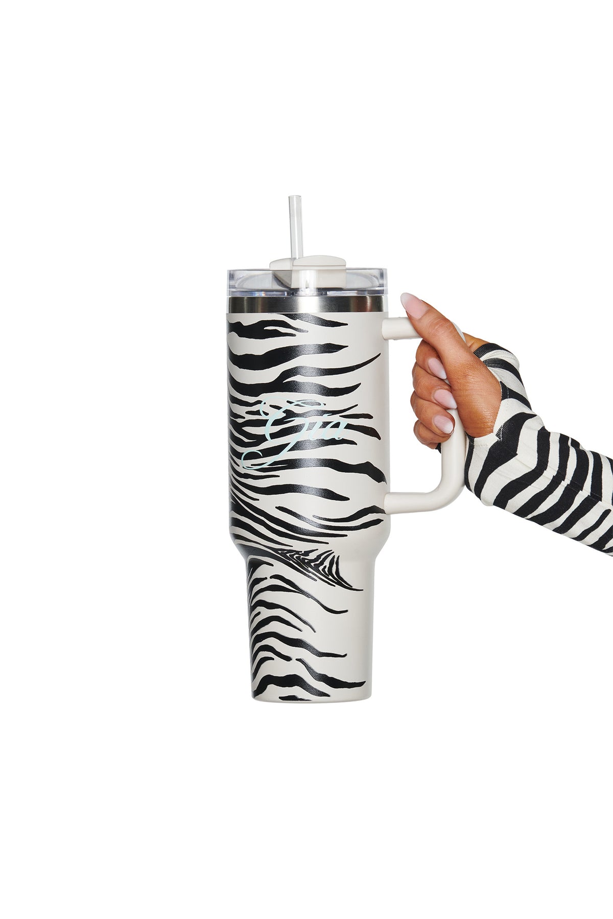 A person wearing a zebra-print sleeve holds a large 40oz I.AM.GIA BLARE CUP - FINE LINE ZEBRA, an insulated stainless steel tumbler with a clear lid and straw, featuring a bold zebra stripe design.