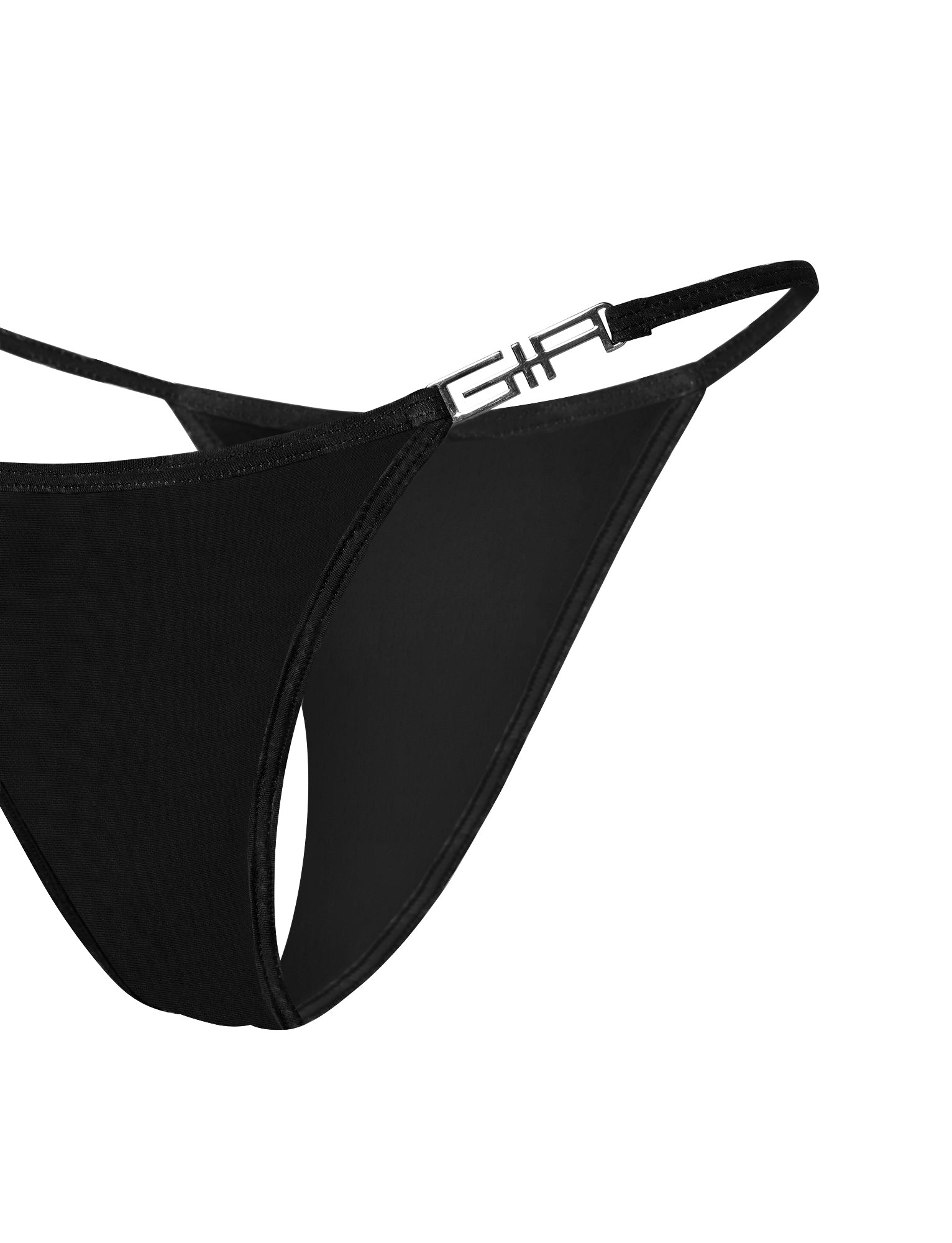 A close-up view of the AVA G-STRING BIKINI BOTTOM - SOLID BLACK by I.AM.GIA, showcasing its sleek and minimalist design with thin straps. The left strap features a small metallic embellishment displaying the letter "F," adding a modern and stylish touch to this black thong. The background is plain and white.