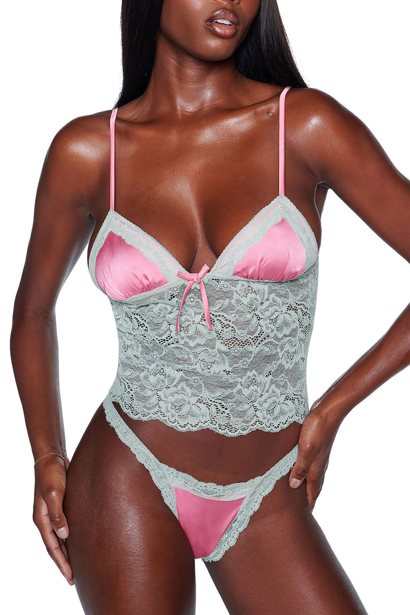 A person is modeling the LOLO 2 PIECE SET - PINK from I.AM.GIA, which features a pink and light green satin lace lingerie combination. This ensemble includes a sheer lace bodice with slender straps and matching underwear, accented with delicate floral details. The image focuses on the upper body and midsection.