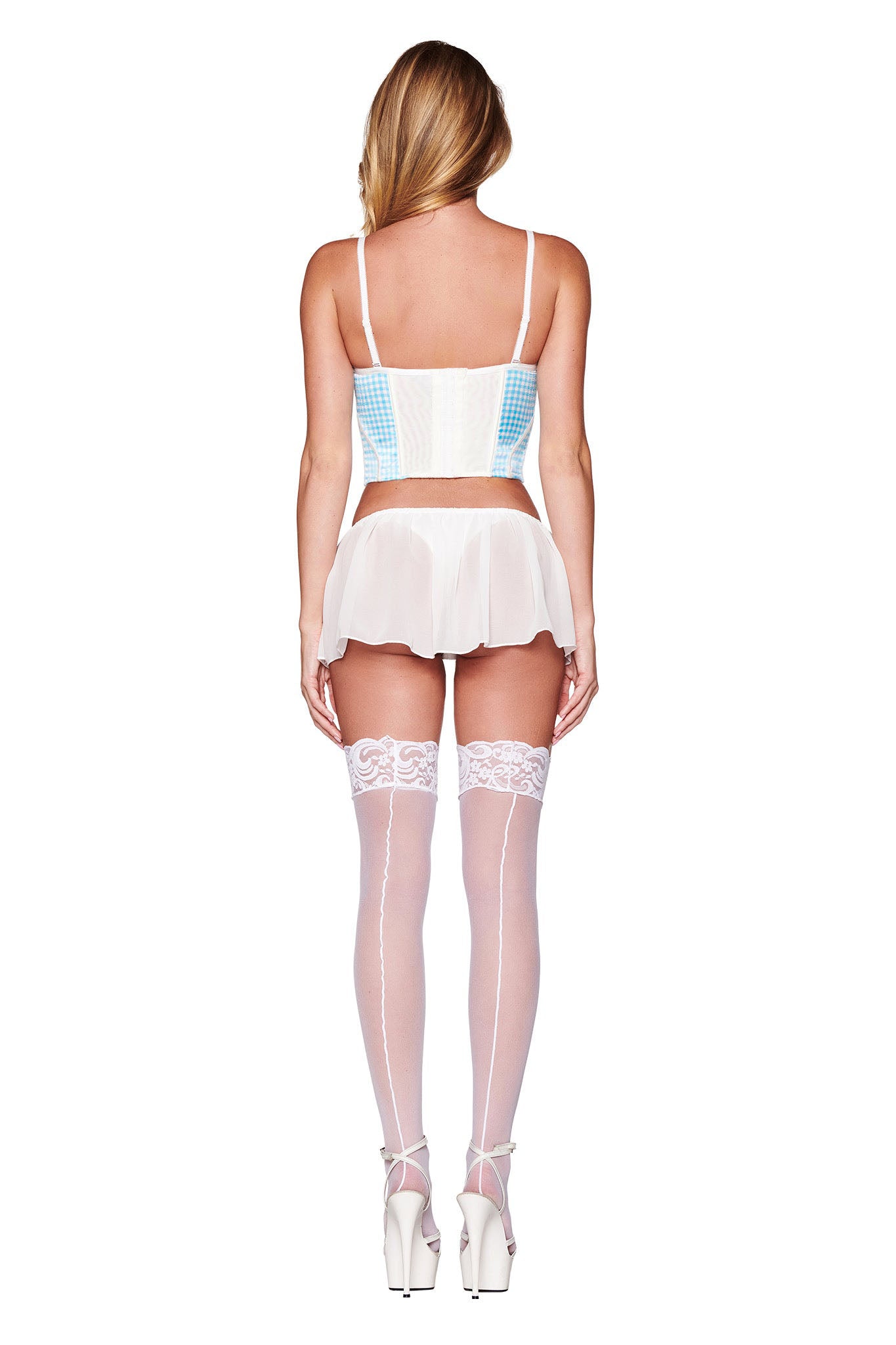 A person with long, wavy blonde hair is seen from the back. They wear the JENNY BUSTIER SET - BLUE : CHECK :GINGHAM by I.AM.GIA, featuring a white corset with light blue accents, a short sheer chiffon skirt, white lace-top thigh-high stockings with a back seam, and white high-heeled shoes.