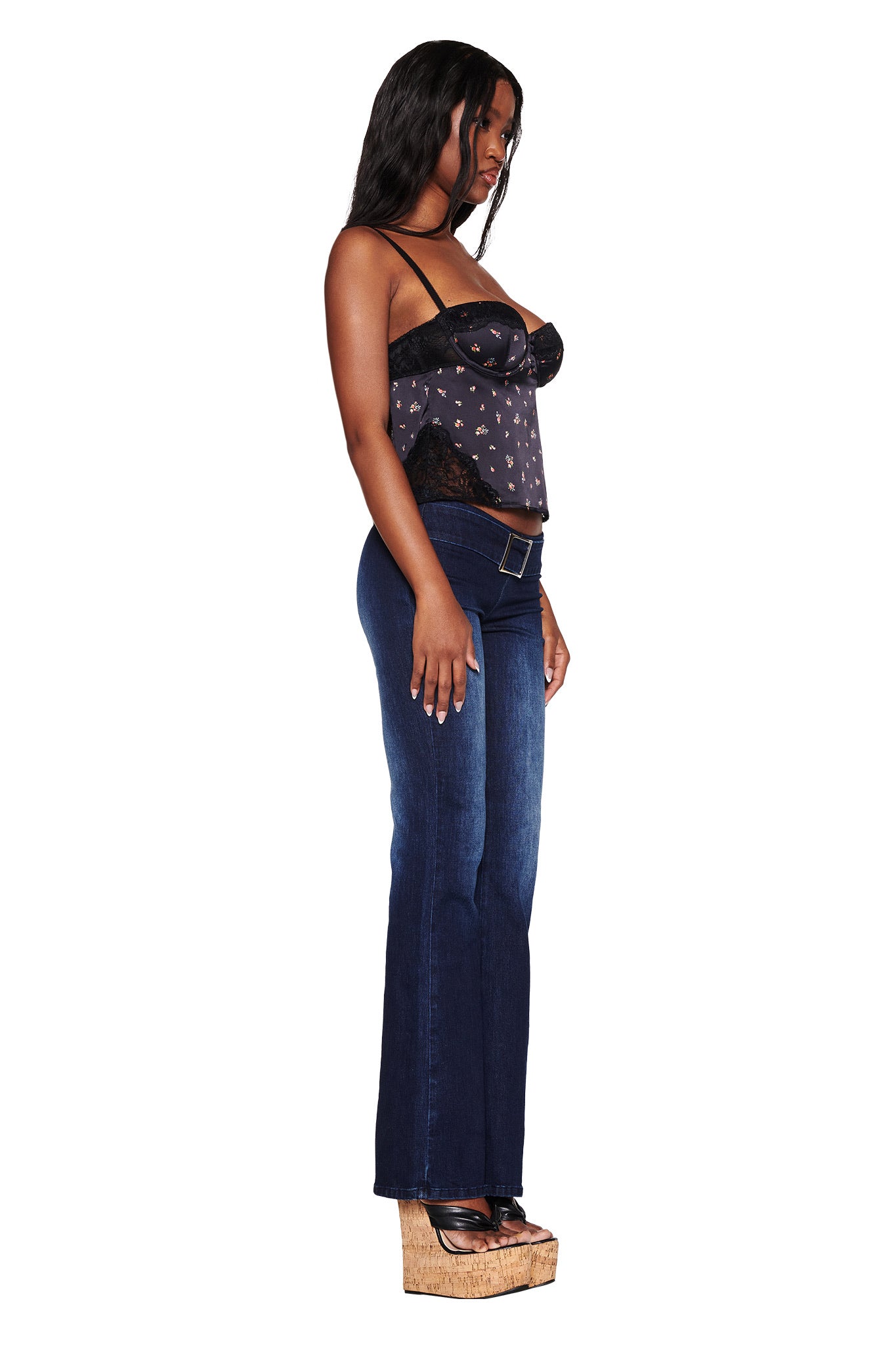 A woman in profile against a white background wears a vintage-inspired black Luella Cami Top with a ditsy floral pattern by I.AM.GIA, paired with dark blue jeans and high wedge sandals. Her hair is long and loose.
