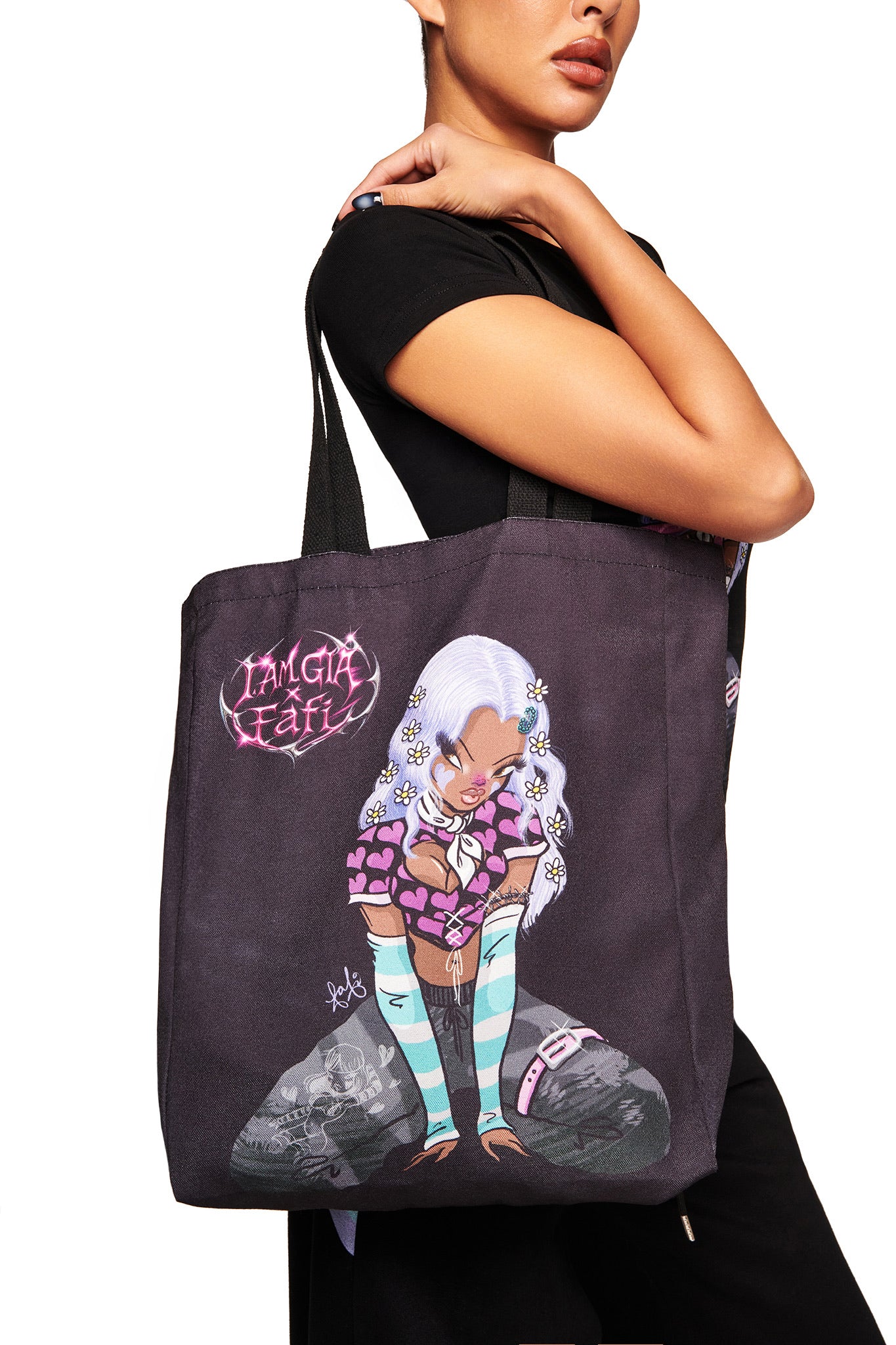 A woman with medium skin holds the I.AM.GIA FAFI TOTE BAG - BLACK, featuring a vibrant cartoon girl with white hair, striped stockings, hearts, and stylized text—an exclusive print from the FAFI collaboration.