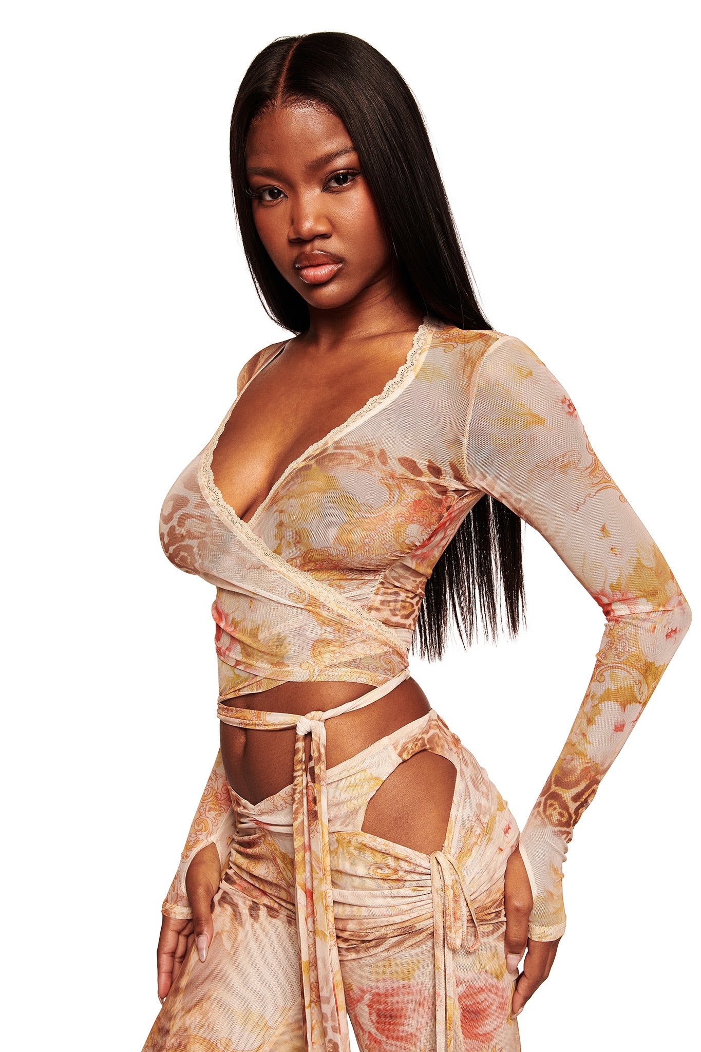 A woman with long, straight hair poses against a white background wearing the I.AM.GIA ERISKA TOP in Desert Rose—a mesh wrap top with scalloped lace trim and matching cut-out pants in soft pastel shades.