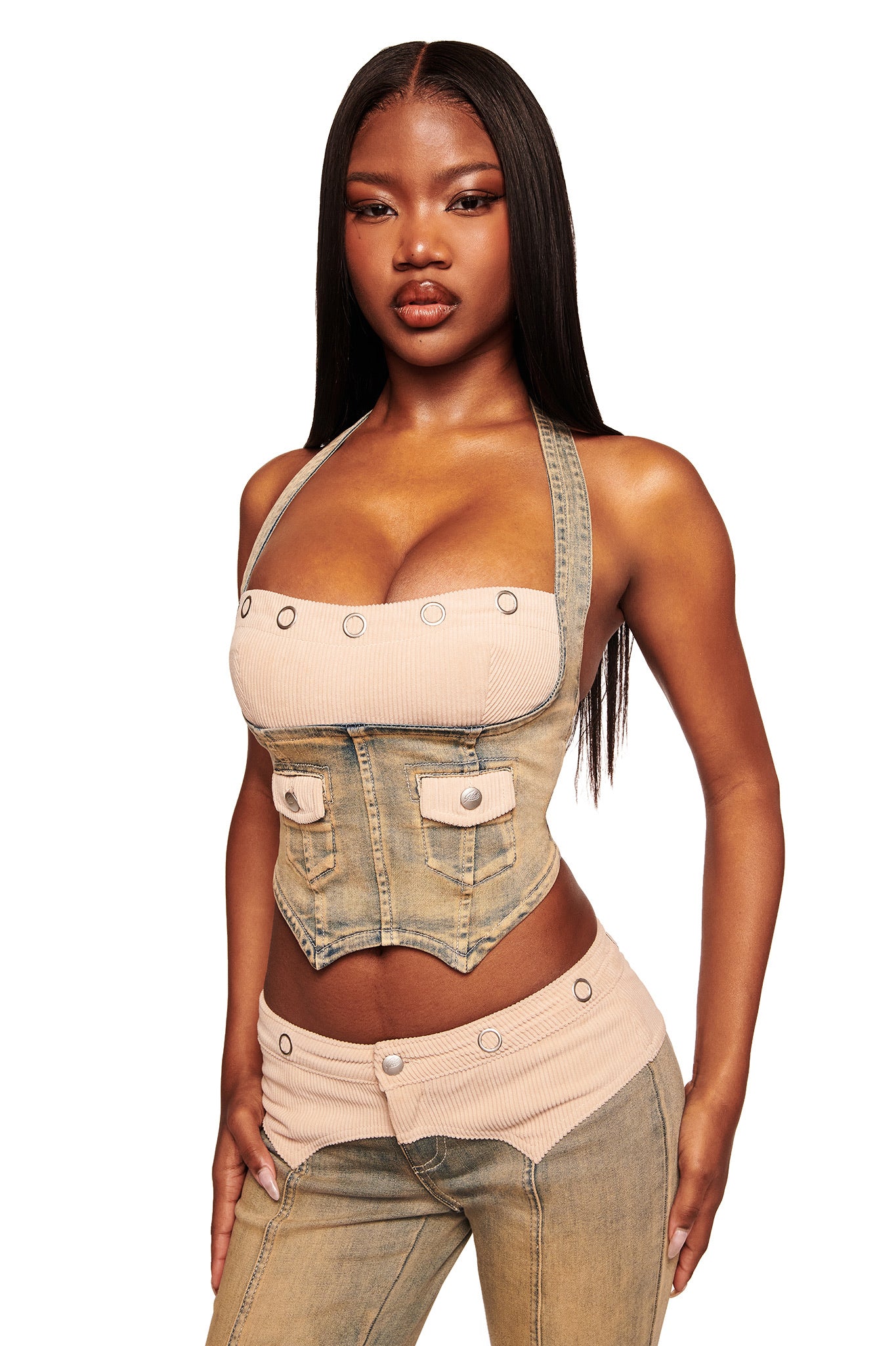 A woman with long straight hair models the I.AM.GIA TOMMIE CORSET in antique denim, featuring a halter neck and button details, paired with matching high-waisted pants. The bodycon fit highlights her figure as she stands against a white background.