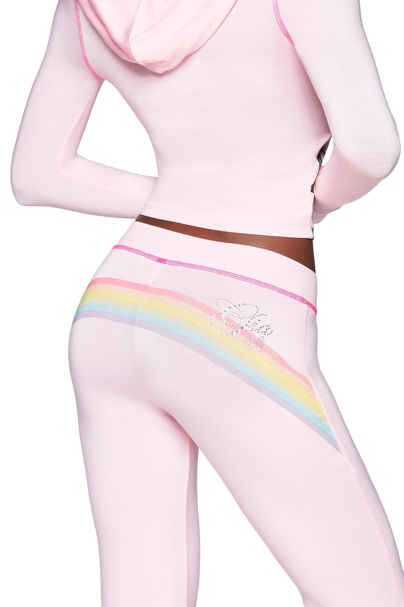 A person shown from the back at waist height wears an I.AM.GIA FAFI BLARE PANT in baby pink, featuring pastel rainbow artwork and rhinestone accents, paired with a matching light pink hoodie.