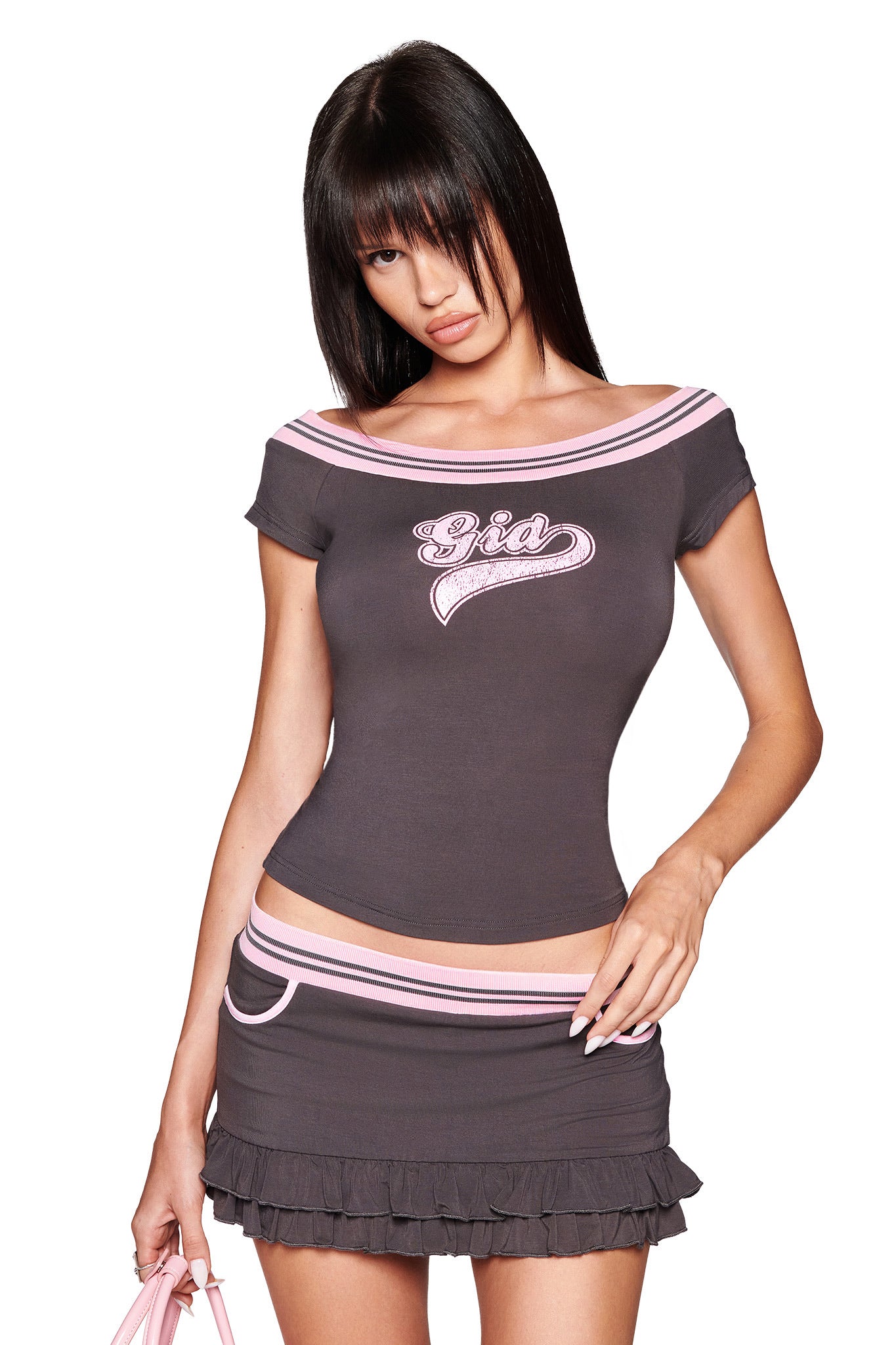 A woman with straight dark hair wears a fitted off-the-shoulder gray top with bubblegum pink elastic trim and "Gia" on it, paired with the ELLIS SKORT - GREY by I.AM.GIA. She holds a pink handbag and poses against a white background.