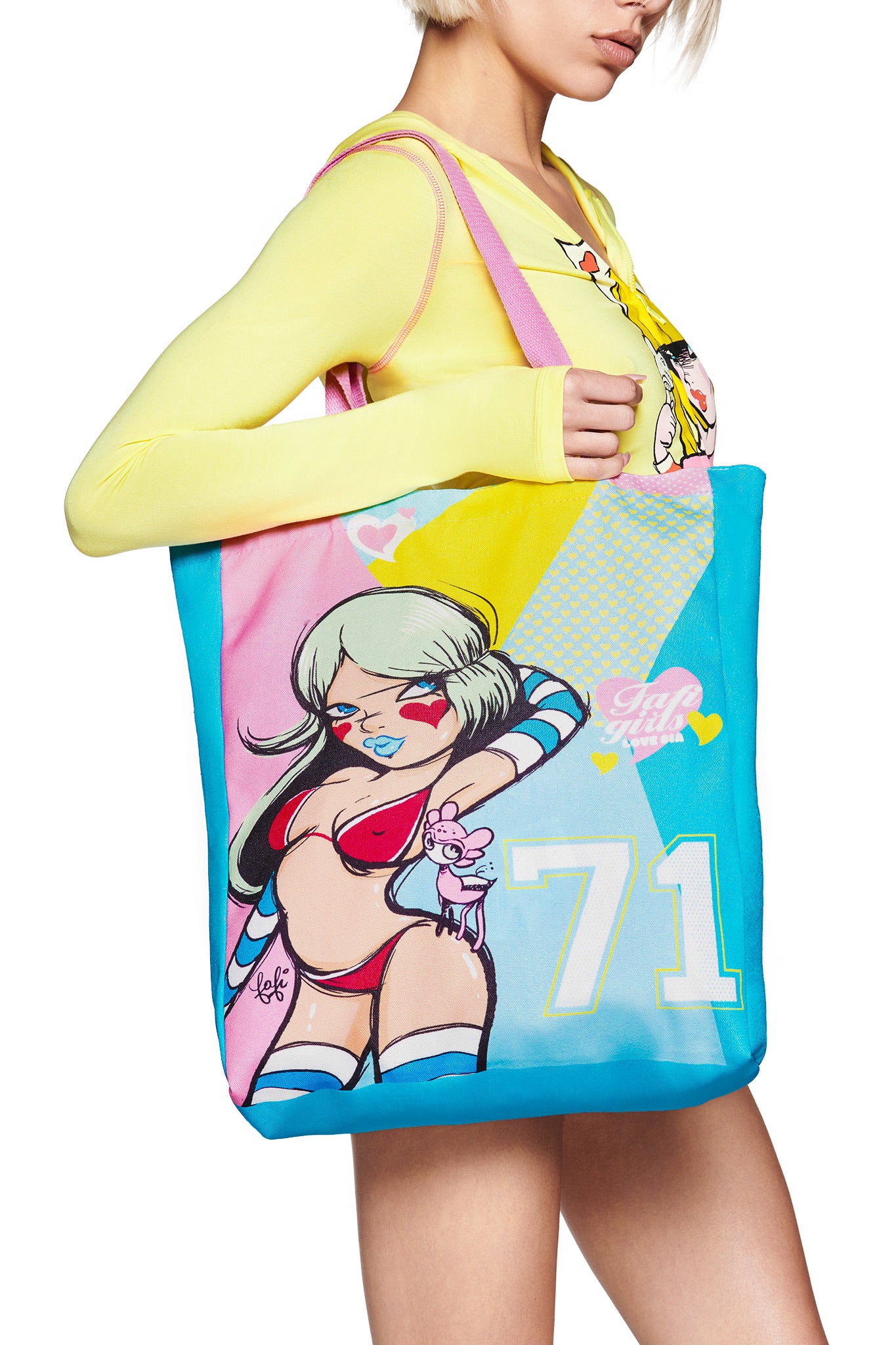 A person in a yellow long-sleeve top holds the I.AM.GIA FAFI TOTE BAG - MULTI, which showcases Fafi artwork of a silver-haired cartoon woman in a red bikini (#71), surrounded by hearts and pastel patterns in pink, blue, and yellow.