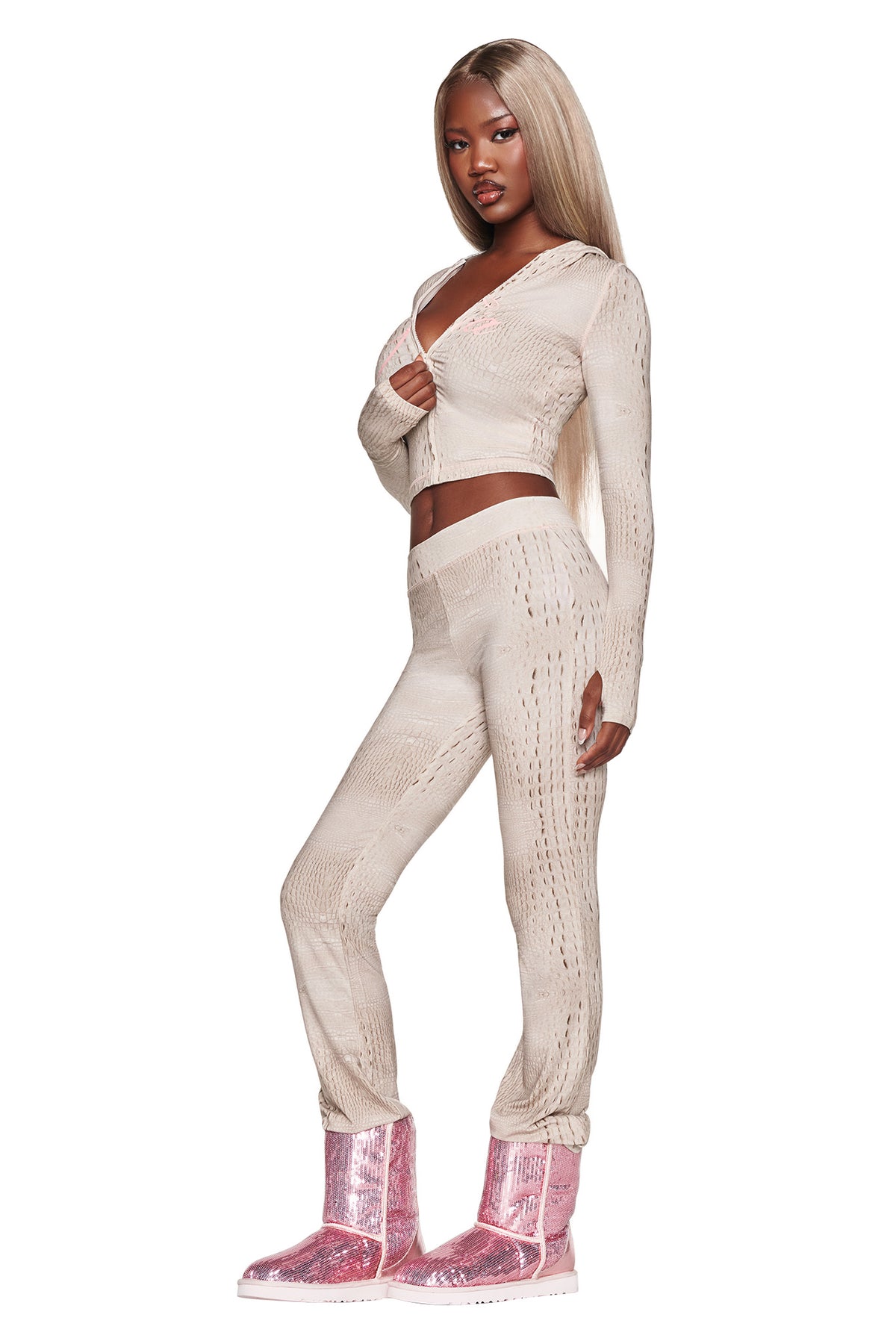 A woman with long blonde hair wears a beige knit crop top and matching I.AM.GIA BLARE TRACKPANT - HOT CROC bamboo trackpants with pink sparkly boots, standing and posing against a white background.