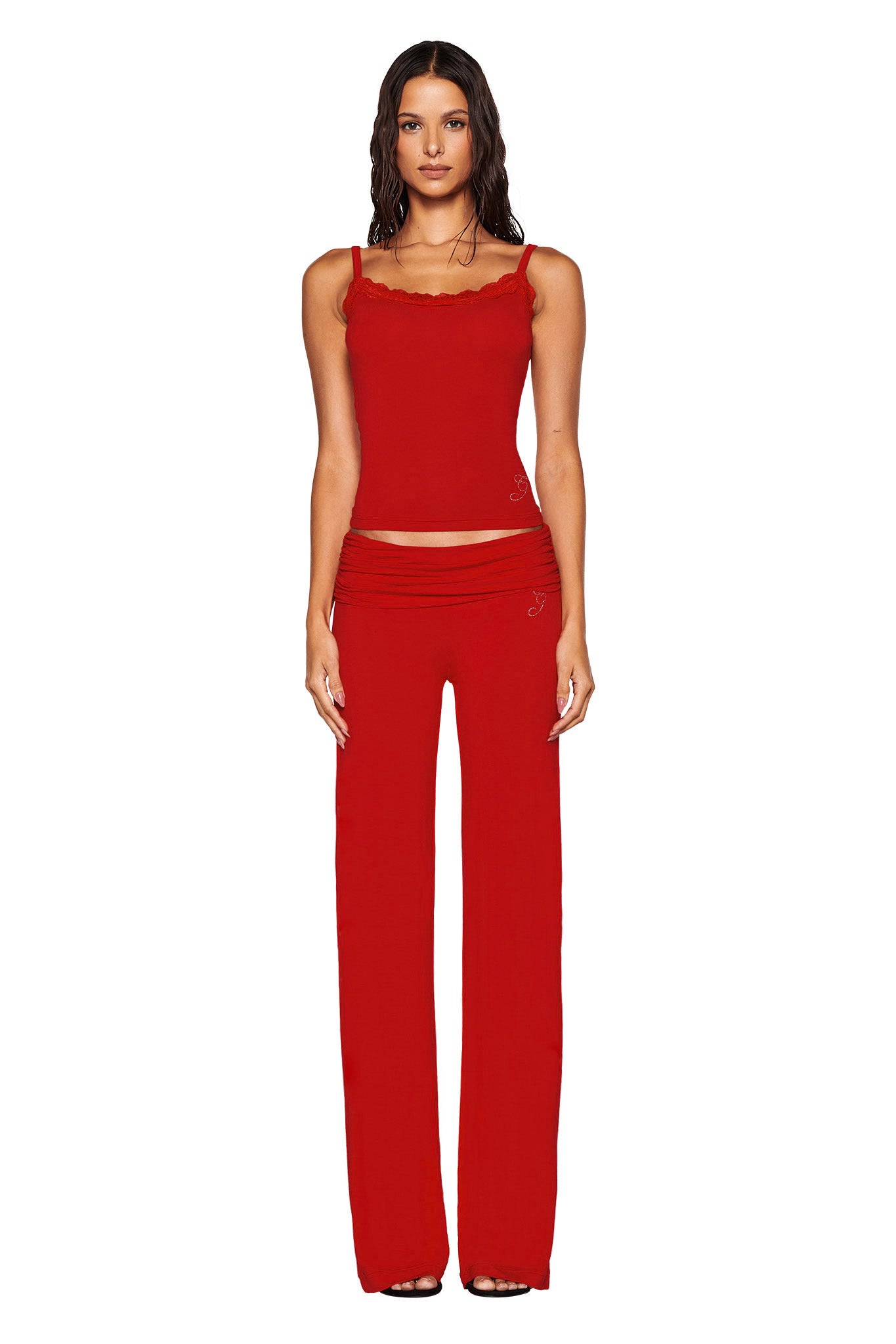 A woman stands on a white background wearing a matching red ensemble, including the I.AM.GIA ERIN TOP - RED with delicate lace trim and wide-leg pants. Her long hair cascades down her shoulders as she gazes forward with confidence.