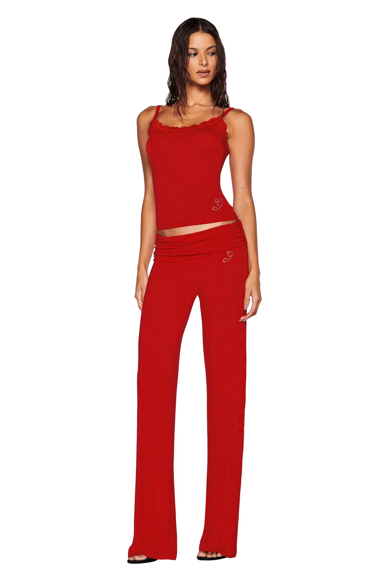 A woman is wearing the red, sleeveless ERIN TOP from I.AM.GIA, featuring frilled edges and paired with matching red pants. The ensemble includes subtle heart designs and a delicate red lace trim. She has long, wavy hair and stands against a white backdrop, highlighting the vibrant bamboo fabric of her outfit.