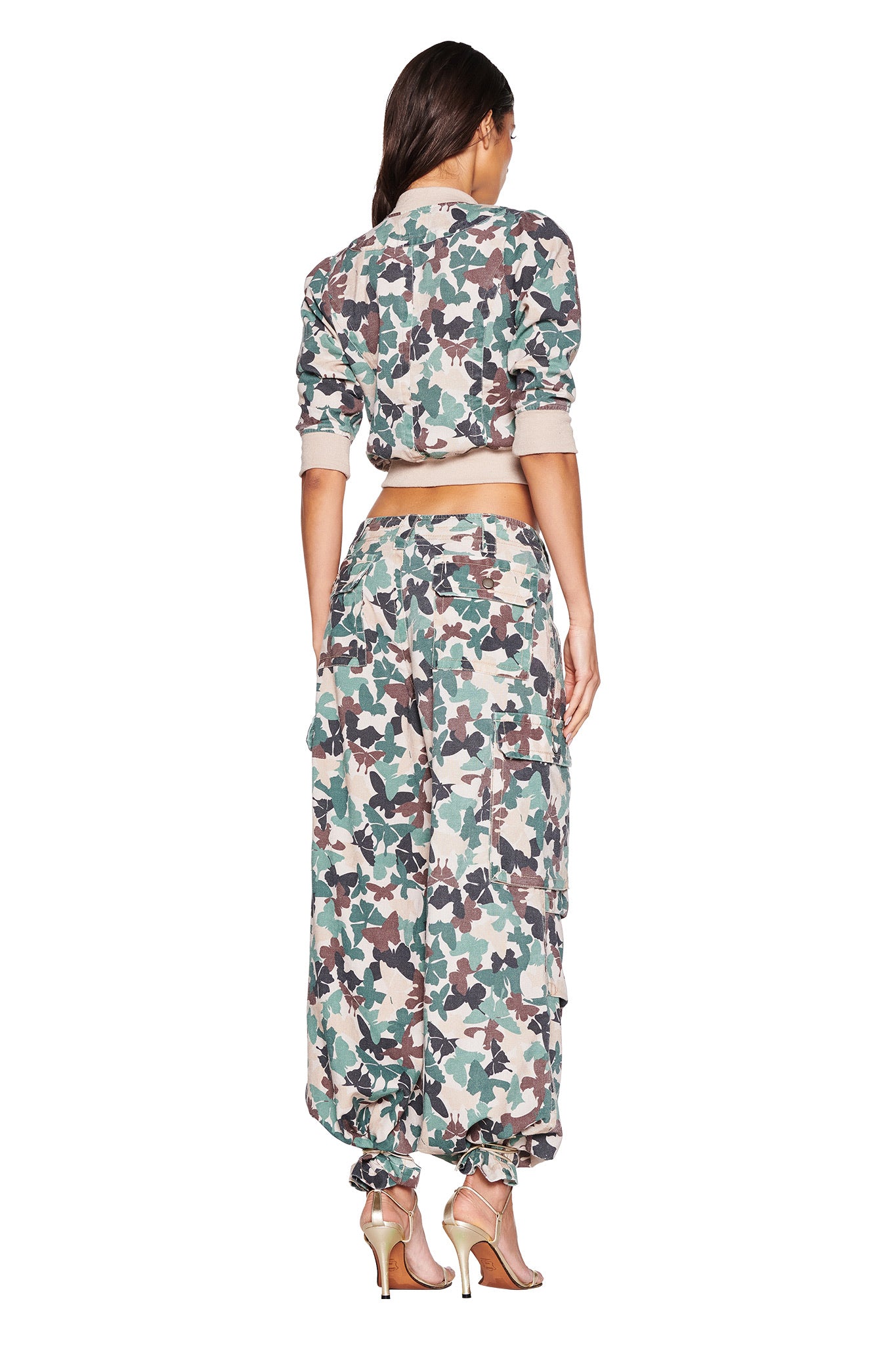A person faces away from the camera, modeling I.AM.GIA's EFFIE CARGO PANT in FLUTTER CAMO with a cropped jacket and completed with high-heeled sandals.