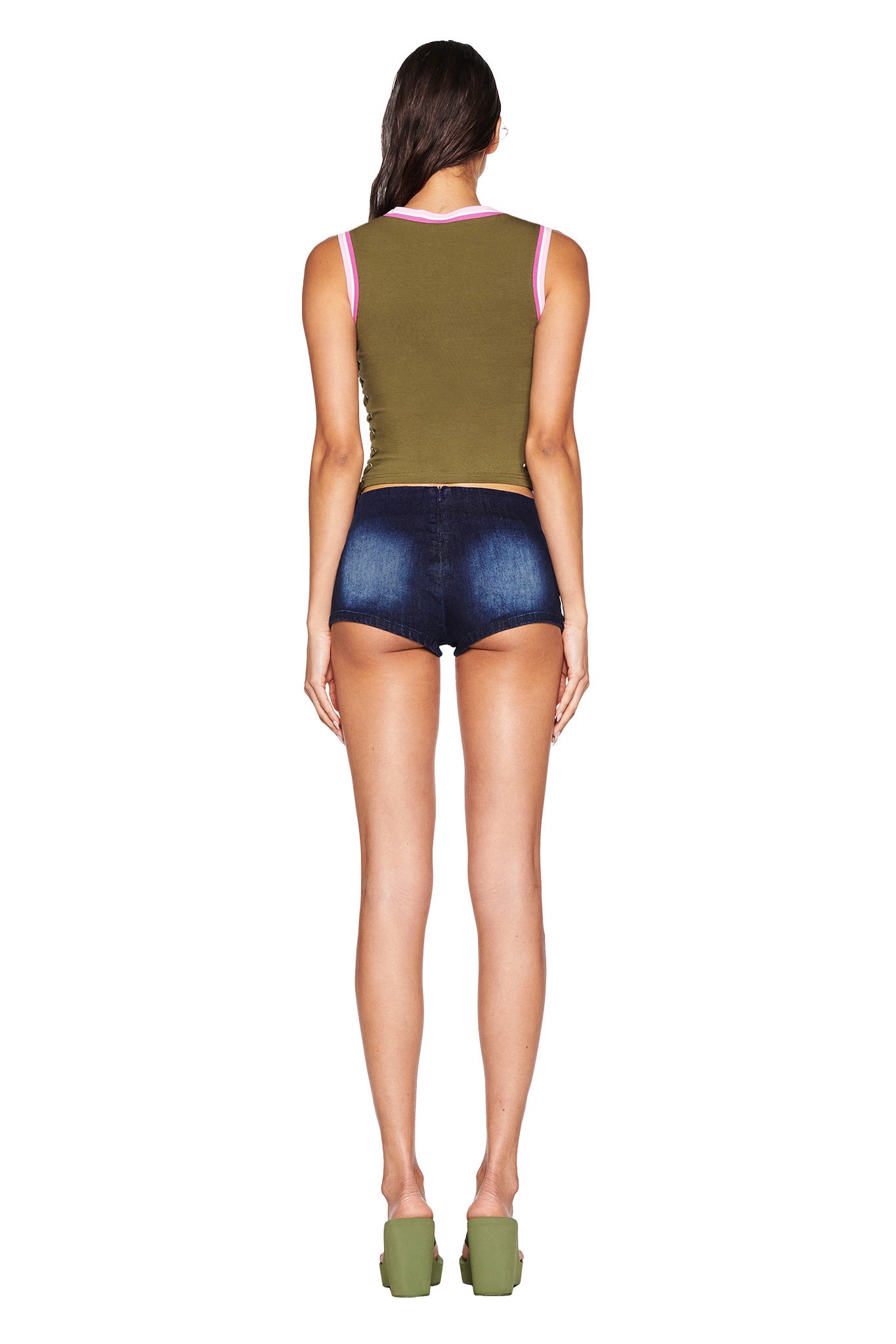 Rear view of a person in I.AM.GIA's NOA TOP - GREEN against a white backdrop, paired with dark blue denim shorts and green platform heels. The corset-style top features pink trim, and their long hair complements the ensemble's elegant bodycon fit.
