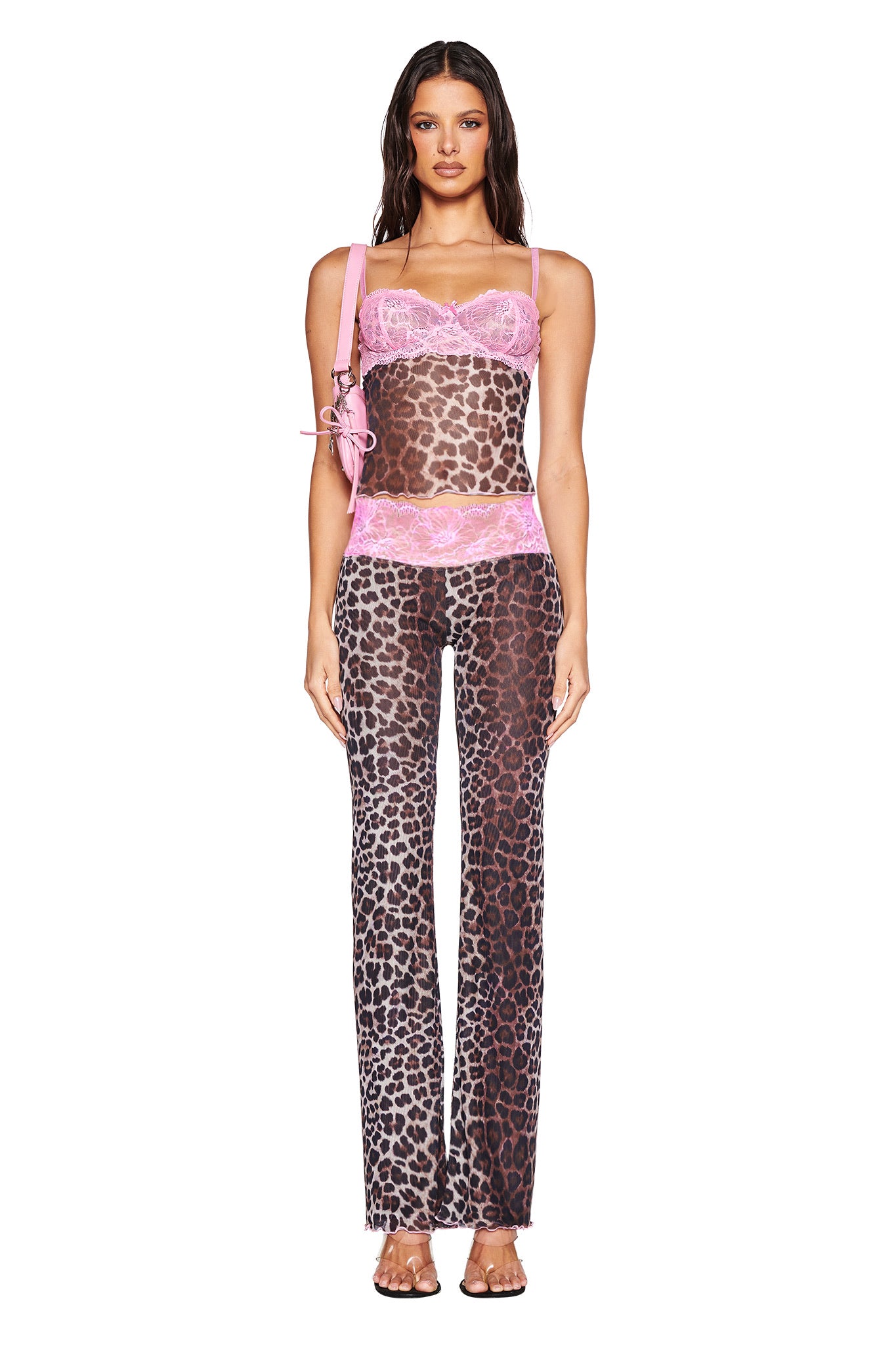A woman faces forward wearing I.AM.GIA’s exclusive SILO PANT in classic leopard print, paired with sheer details, pink lace accents, clear heels, a pink shoulder bag, and her long wavy brown hair flowing.