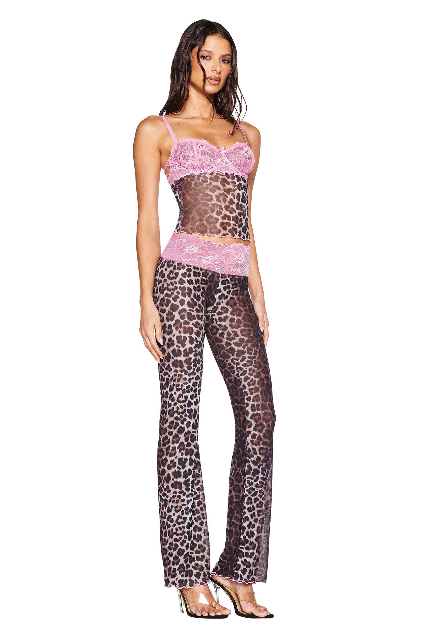 A woman stands against a white background wearing the I.AM.GIA SILO TOP - CLASSIC LEOPARD with matching pants featuring pink lace trim, styled with clear high-heeled sandals.