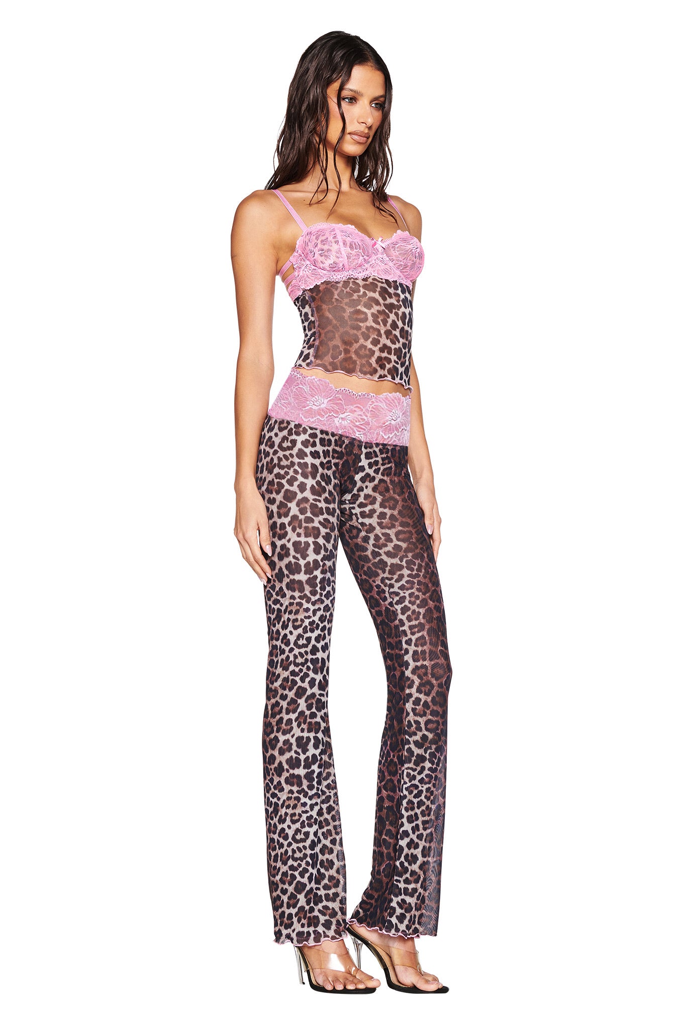 A woman wears the I.AM.GIA SILO PANT - CLASSIC LEOPARD, a sheer leopard-print low-rise pant with pink lace trim, matching camisole, and silver high-heeled sandals.