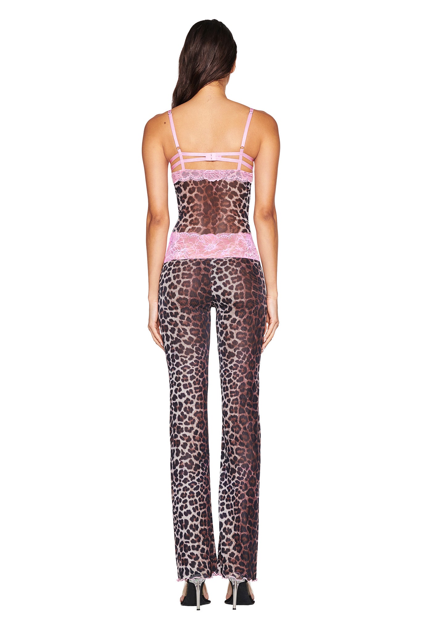 A woman with long brown hair faces away in the I.AM.GIA SILO TOP - CLASSIC LEOPARD, a sheer leopard print mesh camisole with pink lace trim, paired with matching pants and black heels, set against a white background.
