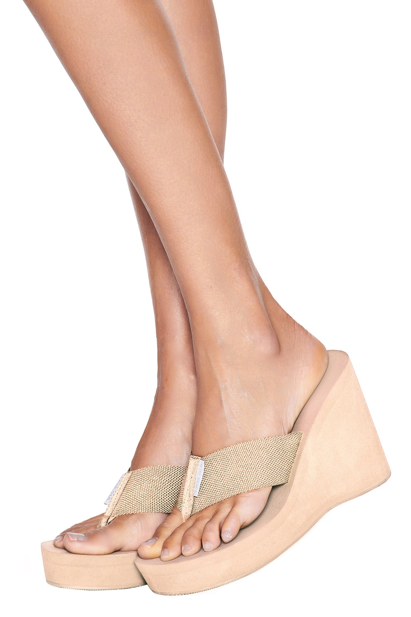 Wearing I.AM.GIA's SHELBY FLIP FLOP - NEUTRAL : TAN, a person stands with one foot slightly crossed over the other against a white background.