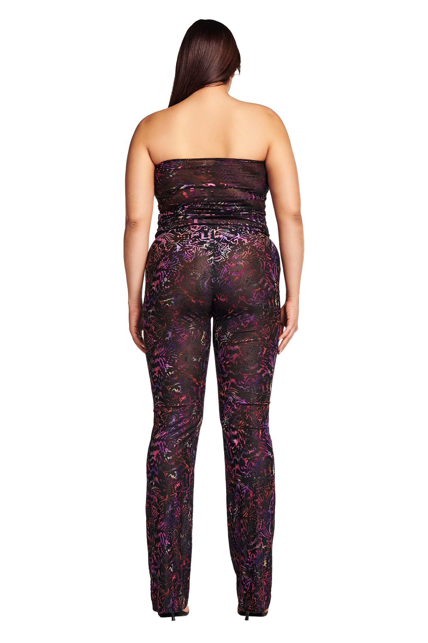 A person is standing with their back to the camera, wearing the AMINA PANT - ANIMAL BURN OUT by I.AM.GIA, characterized by a colorful, abstract design in shades of purple, pink, and blue. Their long hair drapes down their back as they pose against a clean white background.