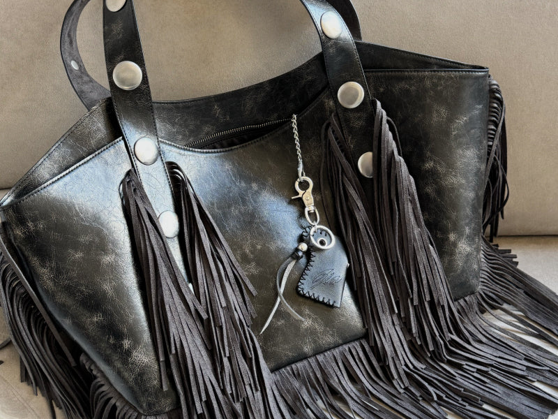 A woman wearing sunglasses and a white, patterned outfit poses on a staircase, holding a white handbag with a furry accessory. Sunlight casts shadows on the beige walls and steps.