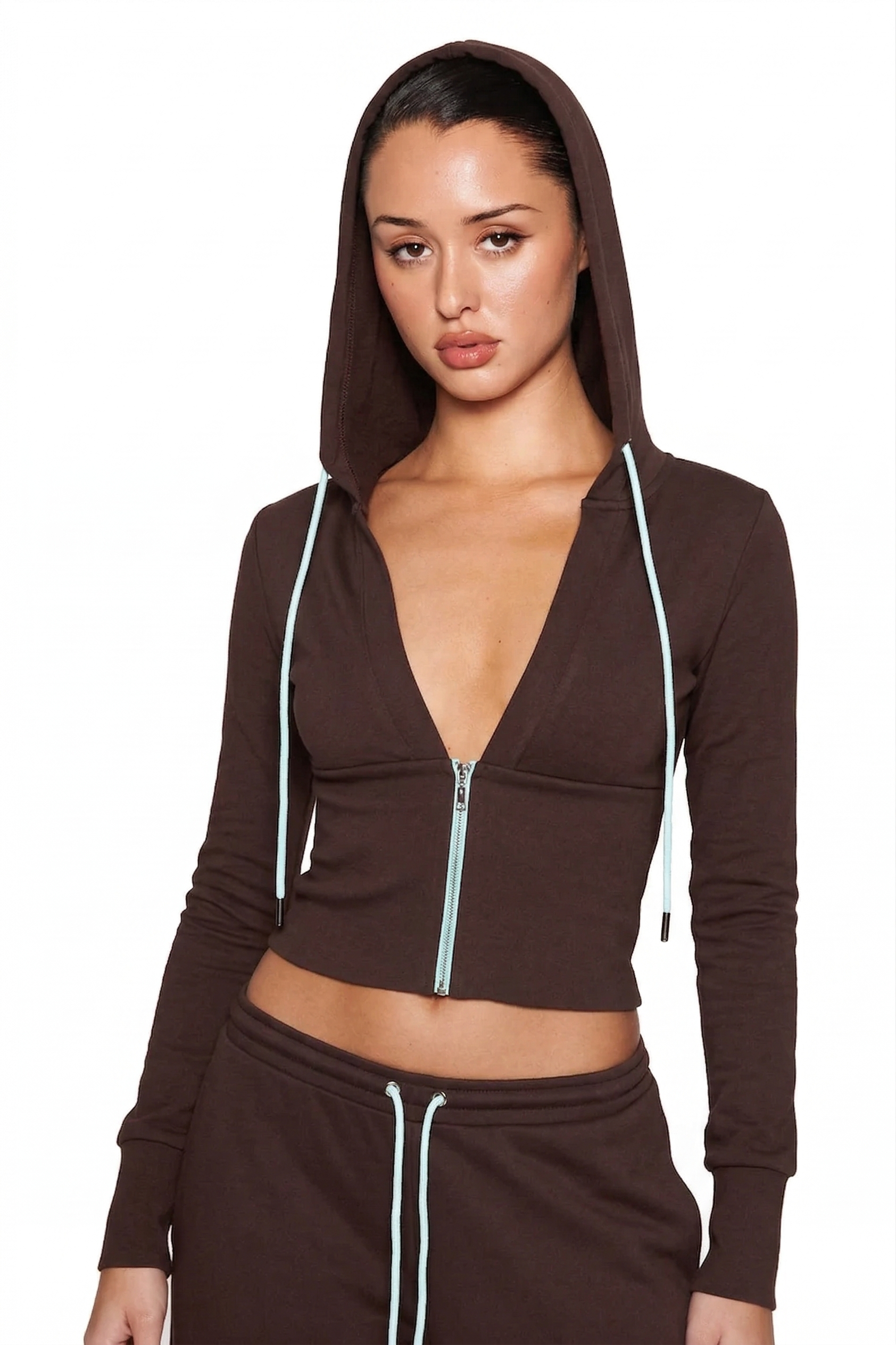 A woman models the I.AM.GIA ARLO LONG SLEEVE TRACK JACKET in brown and blue, featuring a zip-up front, deep V-neck, hood up, light blue drawstrings, and matching pants, posed against a plain white background.