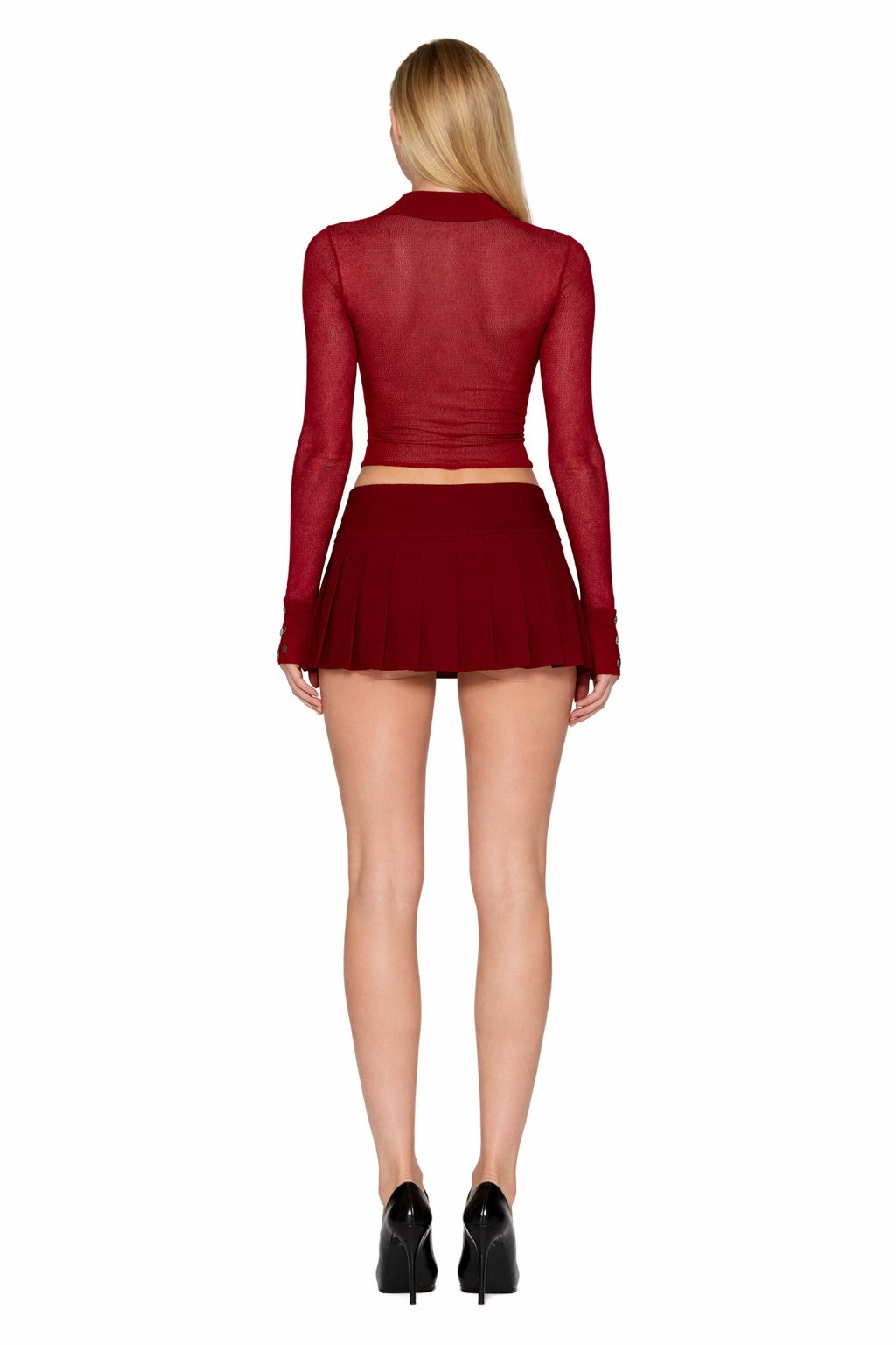 A woman with long blonde hair faces away, wearing the I.AM.GIA DAVINA TOP in wine red, paired with a short pleated red skirt and black high heels against a crisp white background.