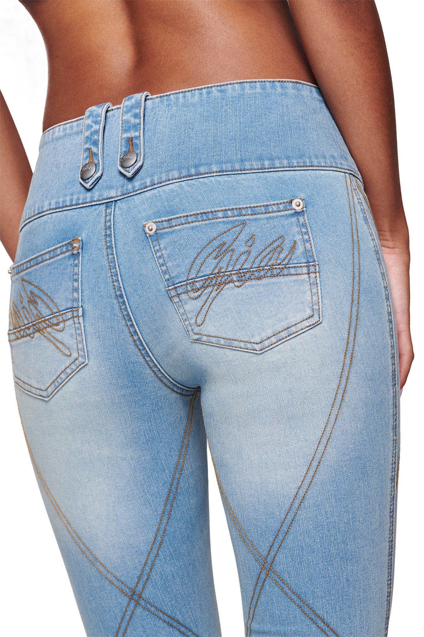 A close-up of a person wearing I.AM.GIA’s MALLORY JEAN - LIGHT BLUE DENIM, featuring brown stitching, decorative belt loops, and “Gia” embroidered on the back pockets. The model’s lower back and upper legs are shown.