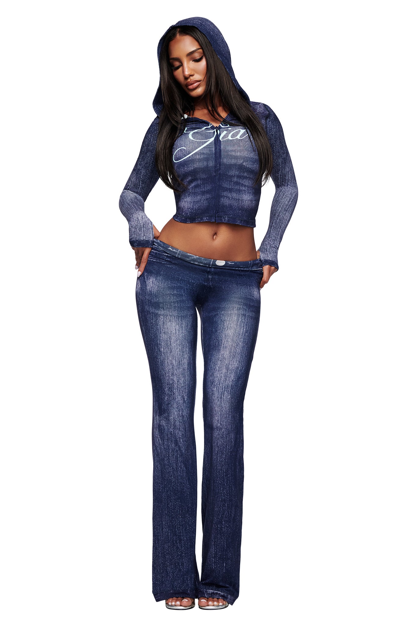 A woman models the I.AM.GIA BLARE TRACKPANT in dark denim with a matching hooded, long-sleeve crop top featuring white chest lettering, posing against a white background.