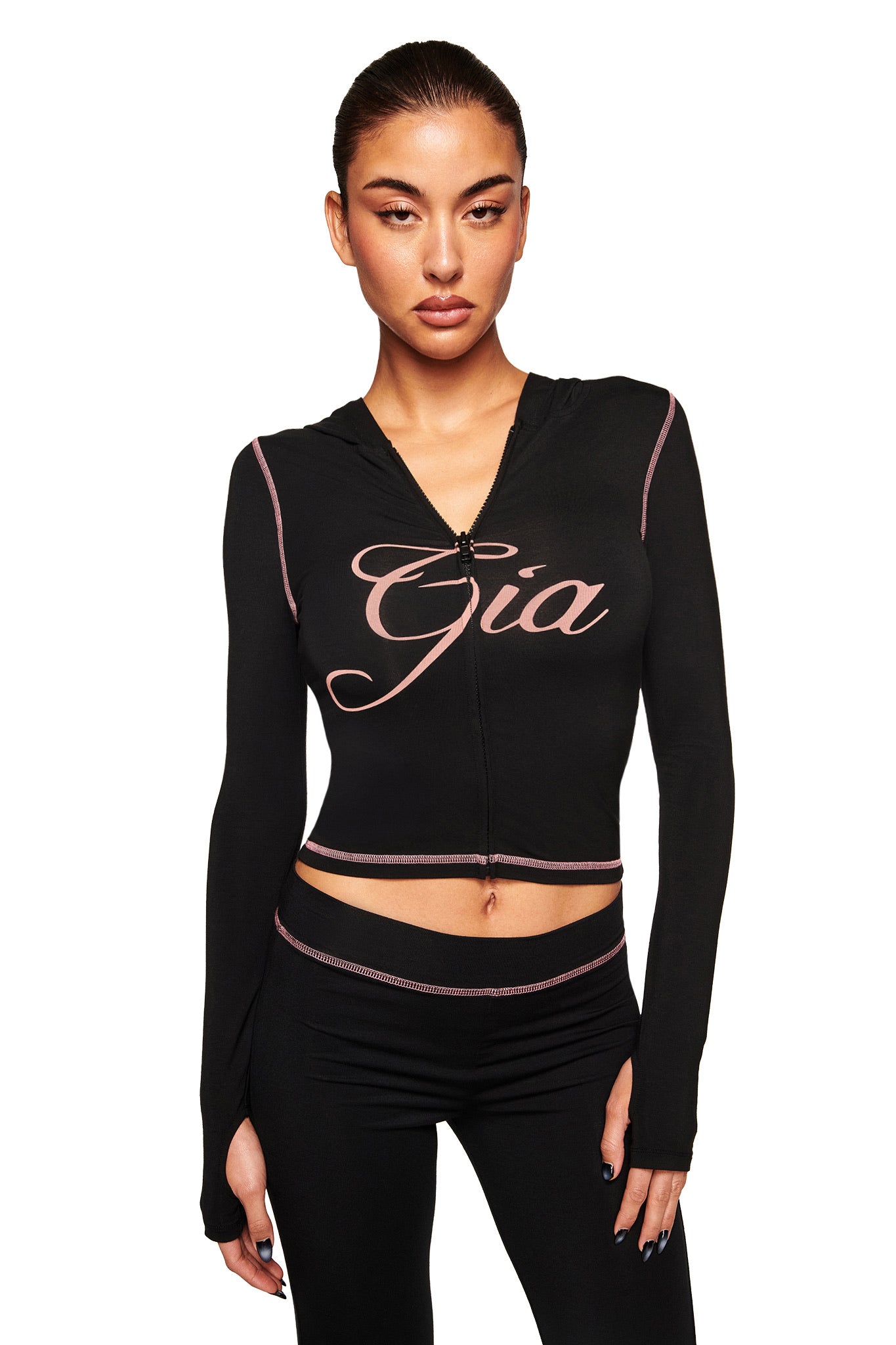 A woman wears the I.AM.GIA BLARE HOODIE in black, featuring "Gia" in bold pink script across the chest, paired with matching black leggings, standing against a plain white background.
