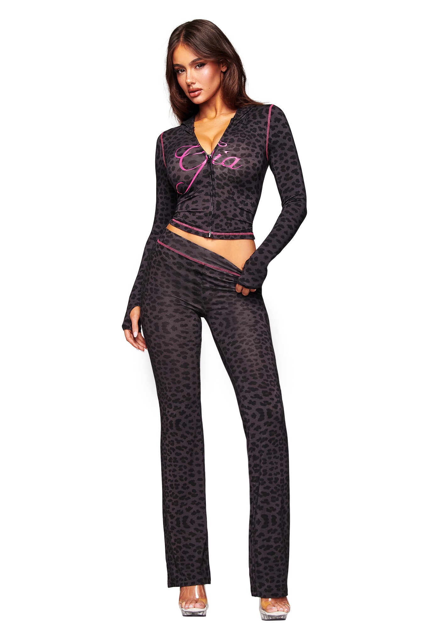 A woman poses against a white background wearing the I.AM.GIA BLARE HOODIE - PANTHER, styled with black high-waisted, leopard-print pants and matching long-sleeve crop top accented with pink, paired with clear high heels.