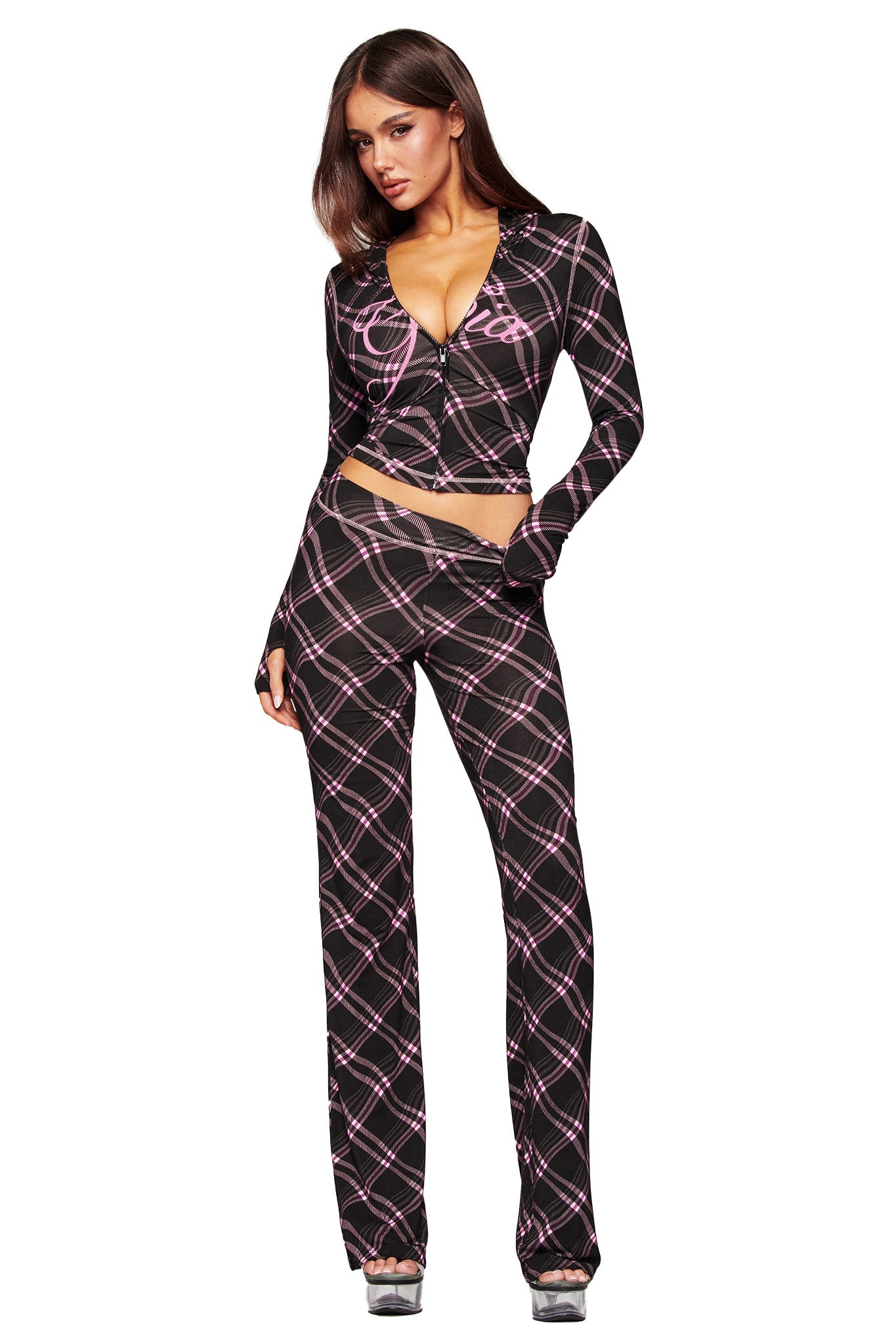 A woman poses in I.AM.GIA's BLARE TRACKPANT - BLACK WARPED PLAID, a high-waisted pant with a pink plaid pattern, styled with a matching fitted long-sleeve crop top and silver heels.