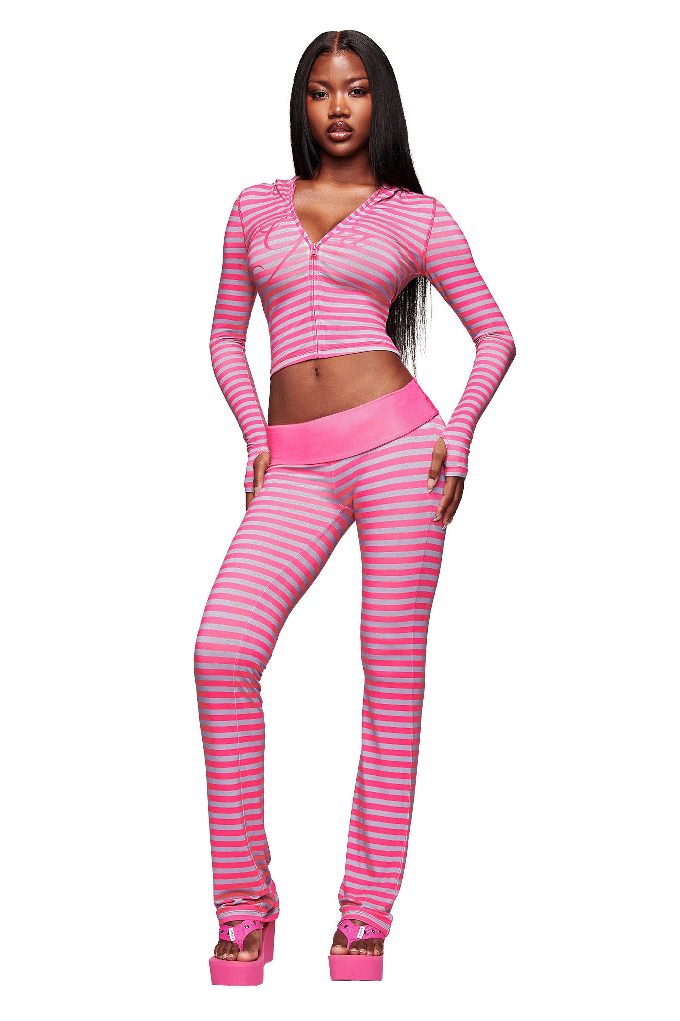A woman poses confidently in the I.AM.GIA BLARE HOODIE - HOT PINK STRIPE with matching flared pants and pink platform heels, set against a white background.