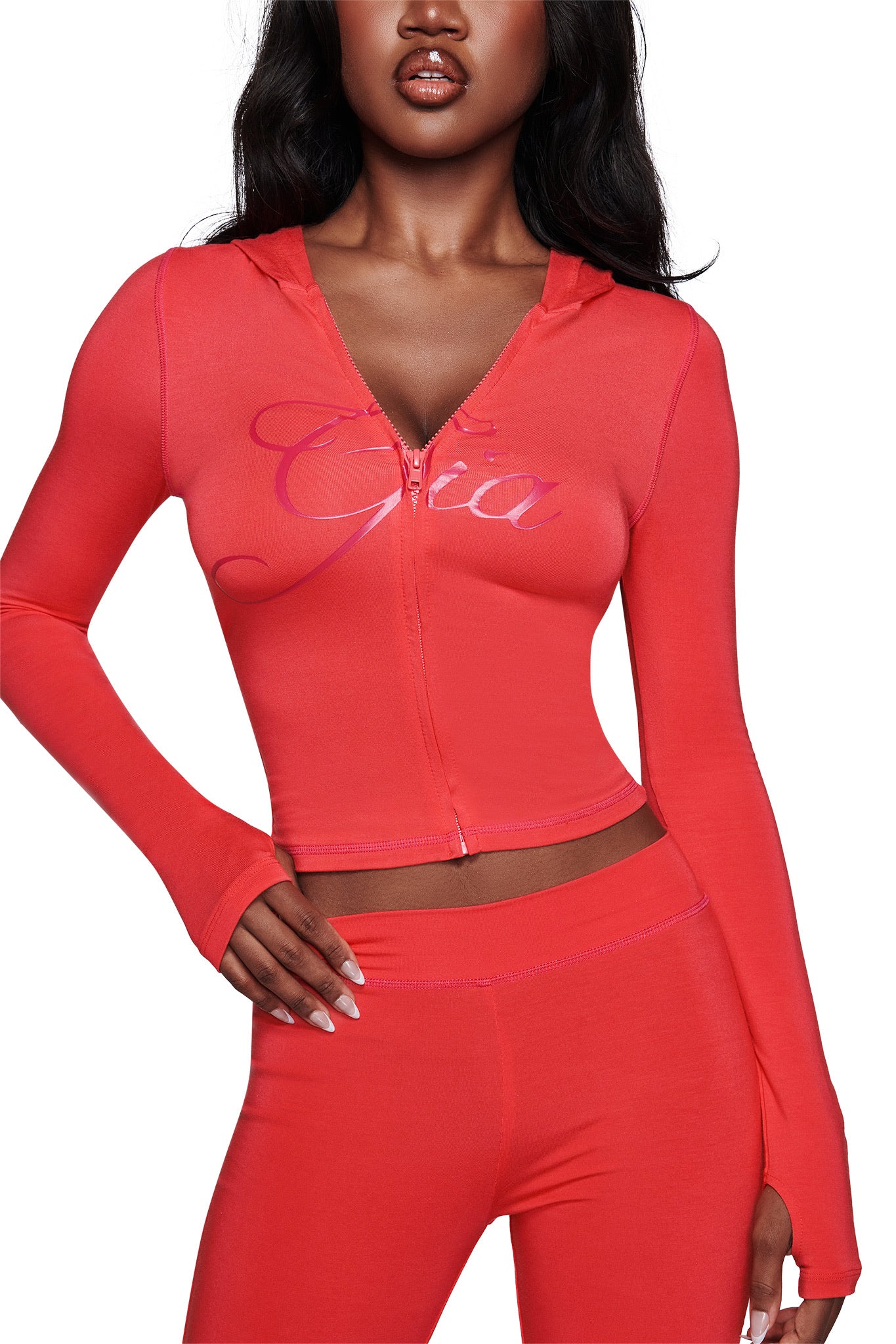 A woman wears a fitted, bright papaya BLARE HOODIE by I.AM.GIA and matching high-waisted leggings, posing confidently with one hand on her hip.