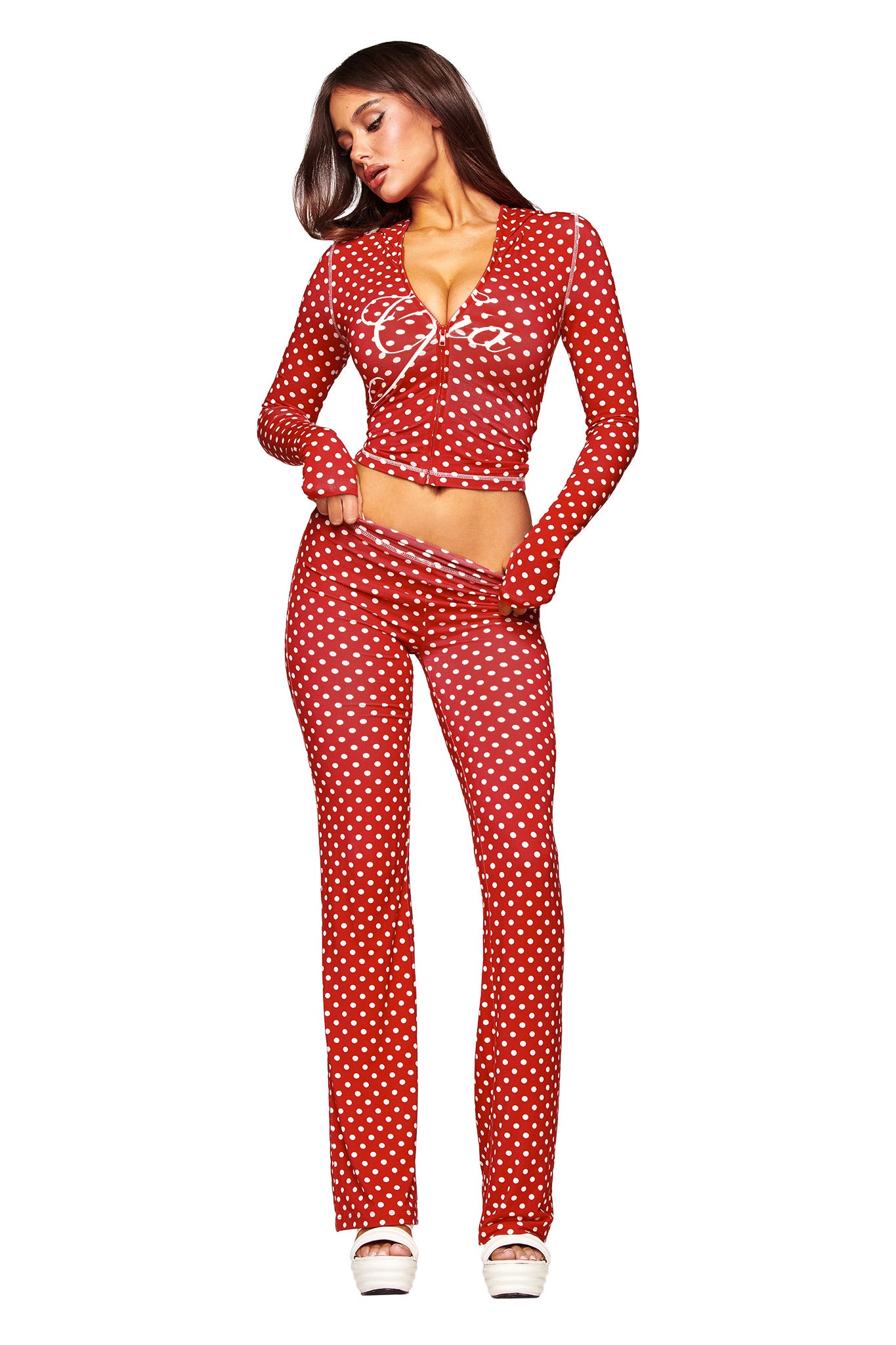 A woman with long hair poses against a white background wearing the I.AM.GIA BLARE HOODIE in red polka dot, matching high-waisted pants, and white platform heels.