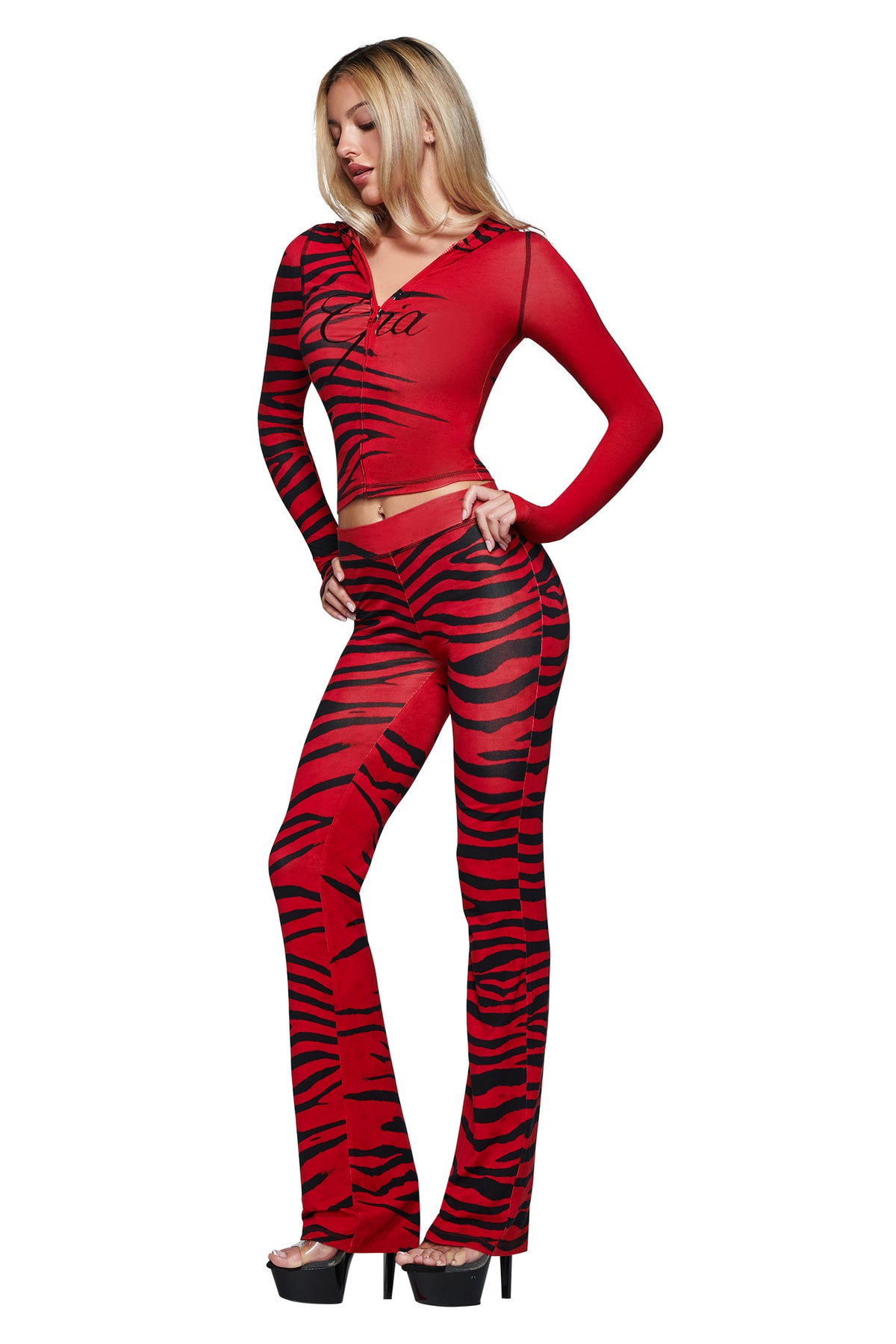 A woman poses against a white background wearing the I.AM.GIA BLARE HOODIE in the Red Wild Side tiger-striped print, paired with matching flared pants and black platform heels.