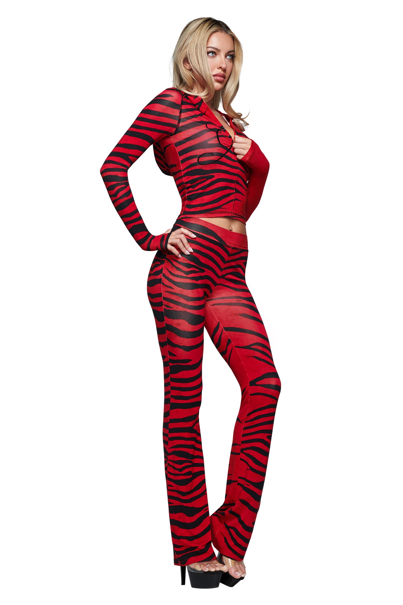 A woman wearing the I.AM.GIA BLARE HOODIE in the bold Red Wild Side print, styled with long sleeves and a fitted silhouette, paired with flared pants and high-heeled shoes, stands against a white background.