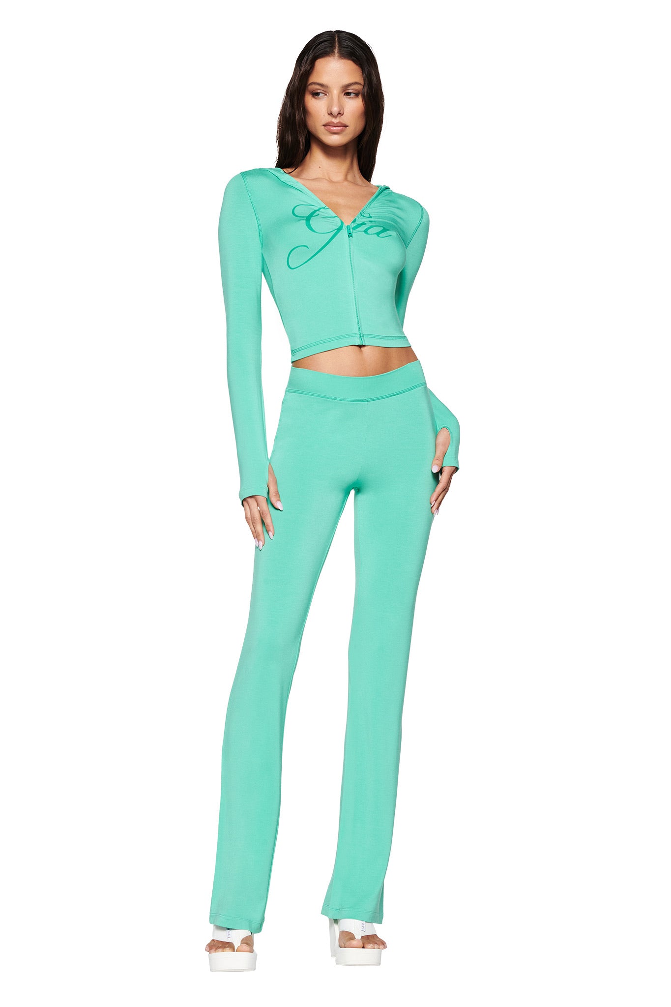 A person stands in an I.AM.GIA BLARE HOODIE, styled in vibrant turquoise teal, paired with matching flared pants and white platform sandals against a plain white background.