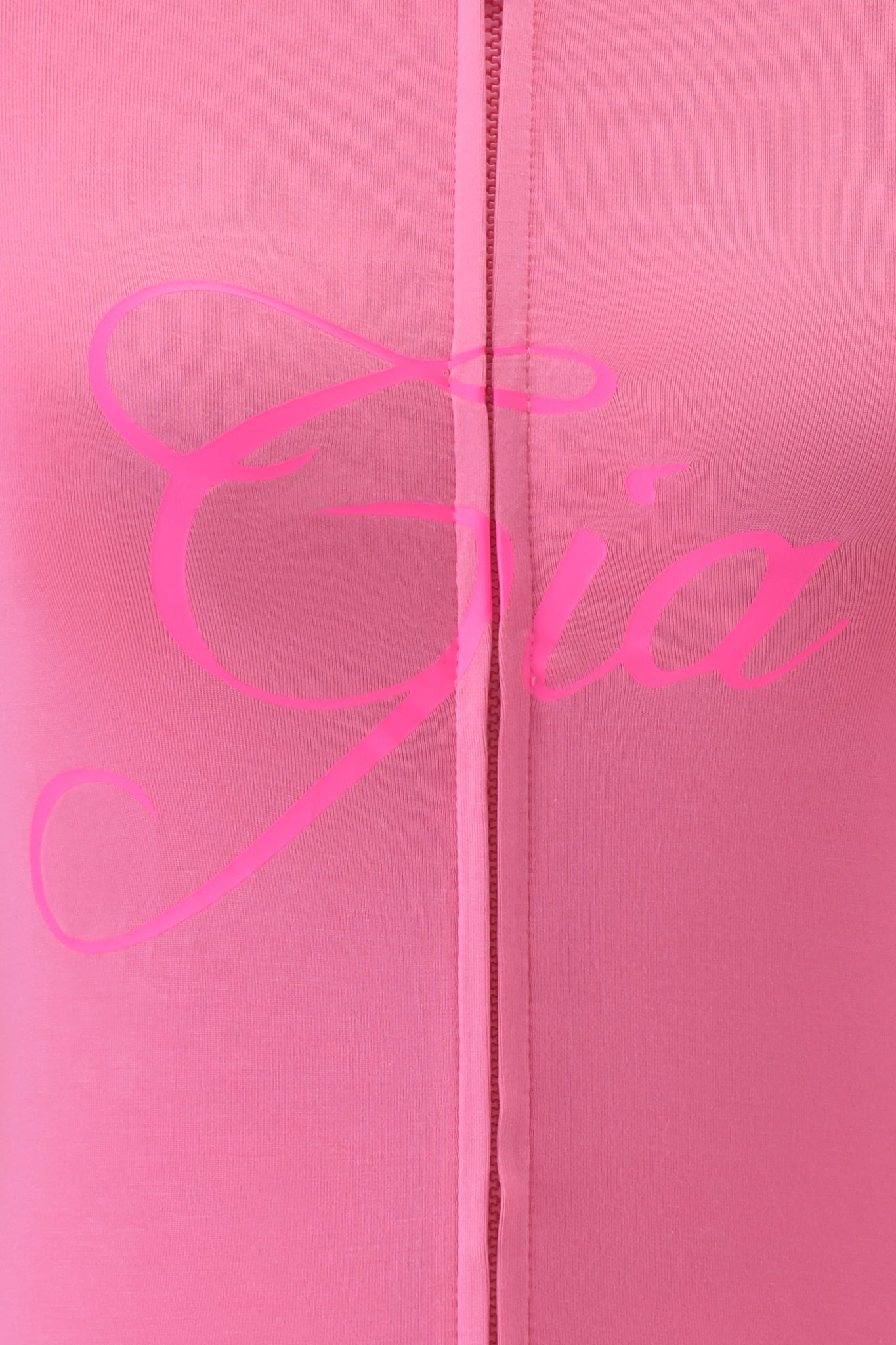 Close-up of neon pink fabric from the I.AM.GIA BLARE HOODIE, featuring a center vertical seam and "Gia" in large cursive pink letters across the bodycon fit.