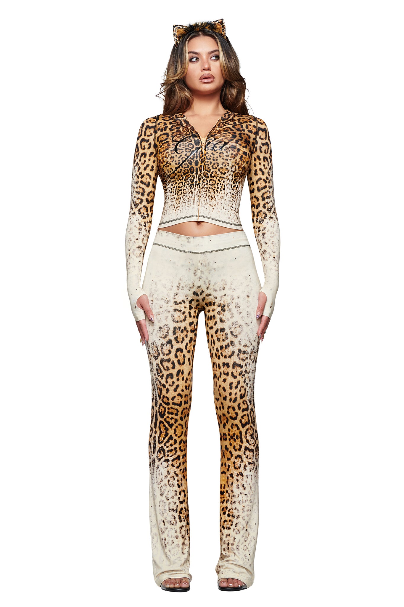 A woman wearing the I.AM.GIA BLARE TRACKPANT in Cream Faded Panthera with a matching zip-up top and cat ears stands against a white background.