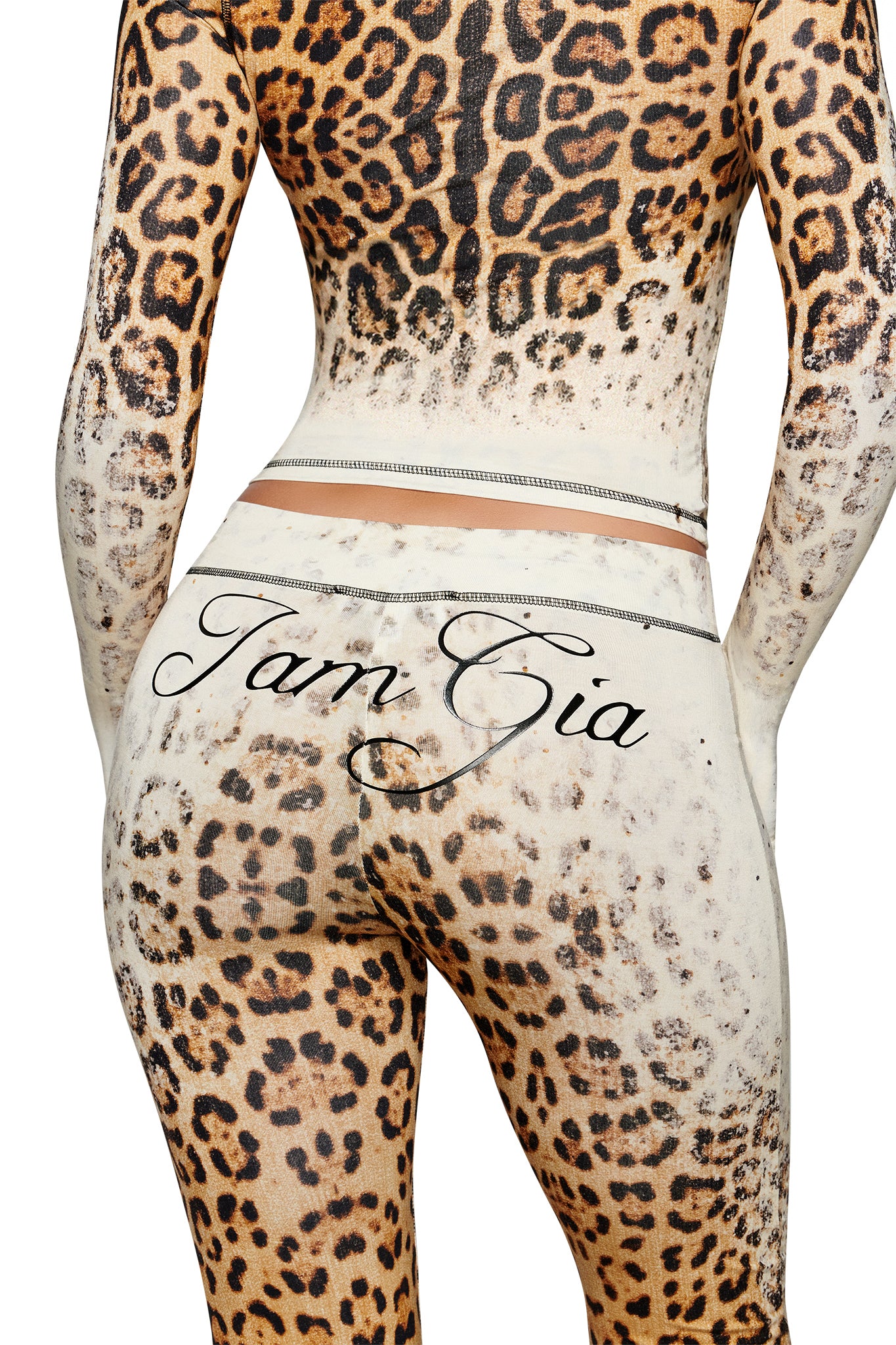A person wearing the BLARE TRACKPANT by I.AM.GIA in Cream Faded Panthera, featuring a bold leopard print and the brand’s script logo displayed across the lower back and upper buttocks. Reminiscent of stylish cheetah print trackpants, the image is cropped to show only the back, from shoulders to thighs.
