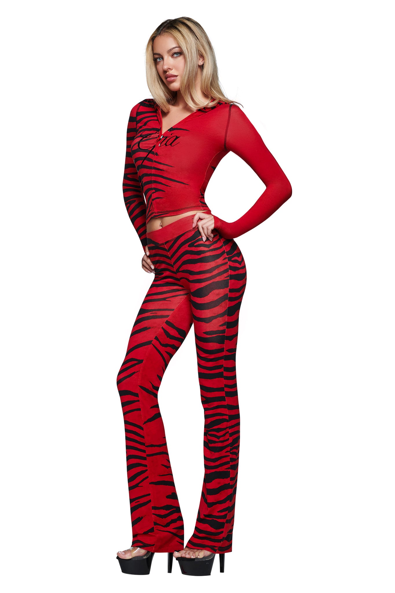 A woman wearing the I.AM.GIA BLARE HOODIE in the bold Red Wild Side print—featuring red and black tiger stripes—poses in high heels against a white background.