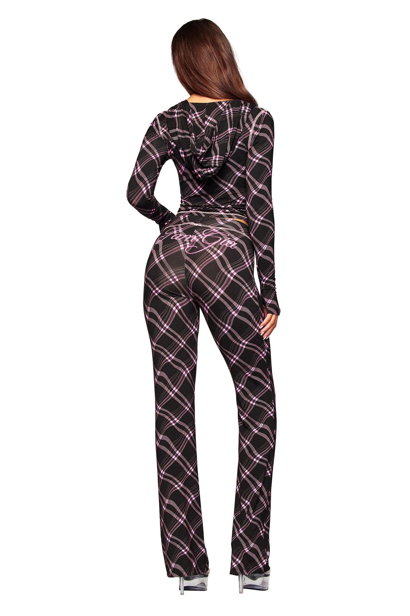 A woman faces away wearing the I.AM.GIA BLARE TRACKPANT in black warped plaid bamboo, with "Baby" in pink on the back, paired with high-heeled clear platform shoes.
