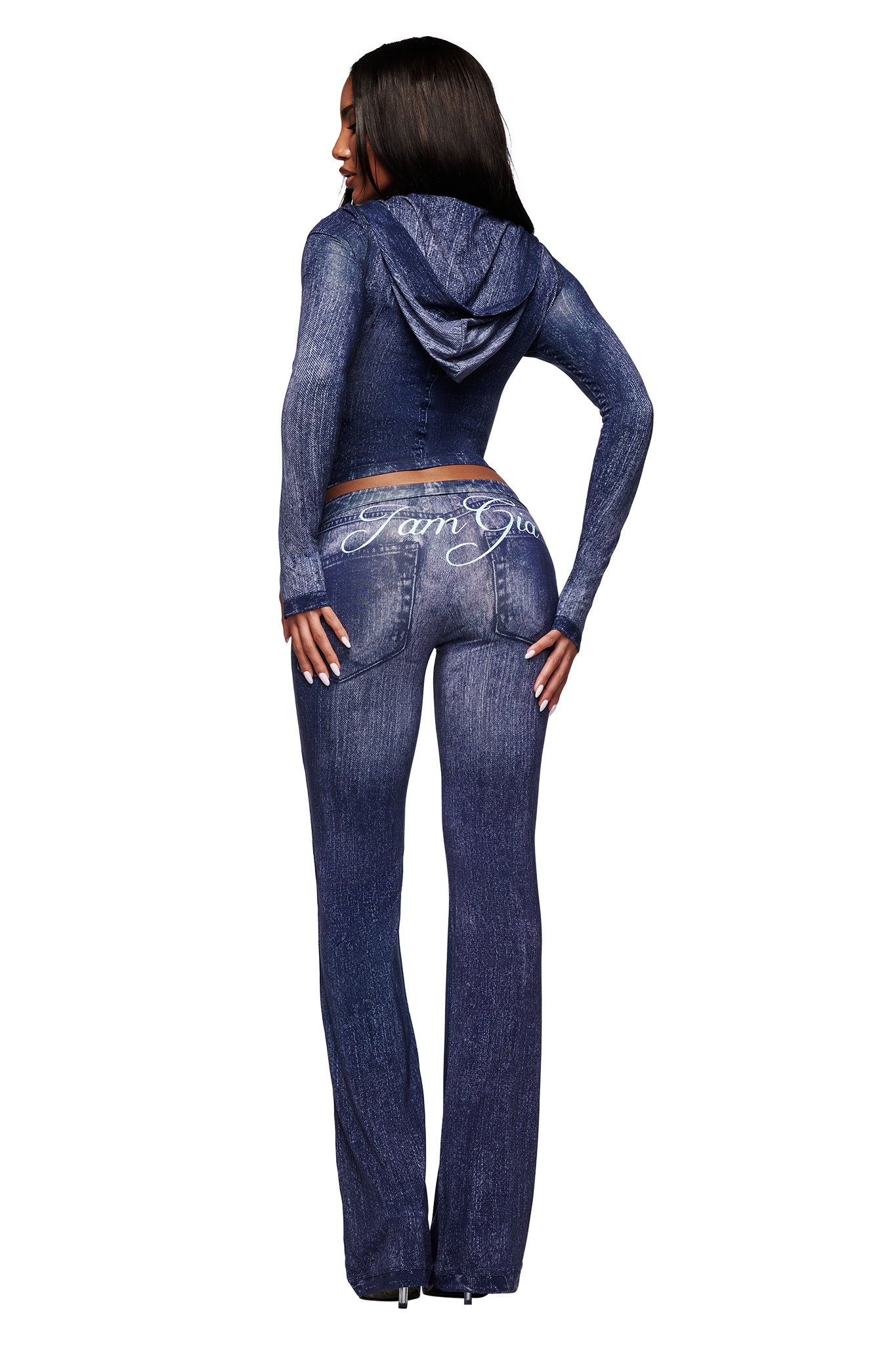 A woman faces away, wearing the I.AM.GIA BLARE HOODIE - DARK DENIM and matching pants with white script on the back. The set features a Dark Denim print against a plain white background.