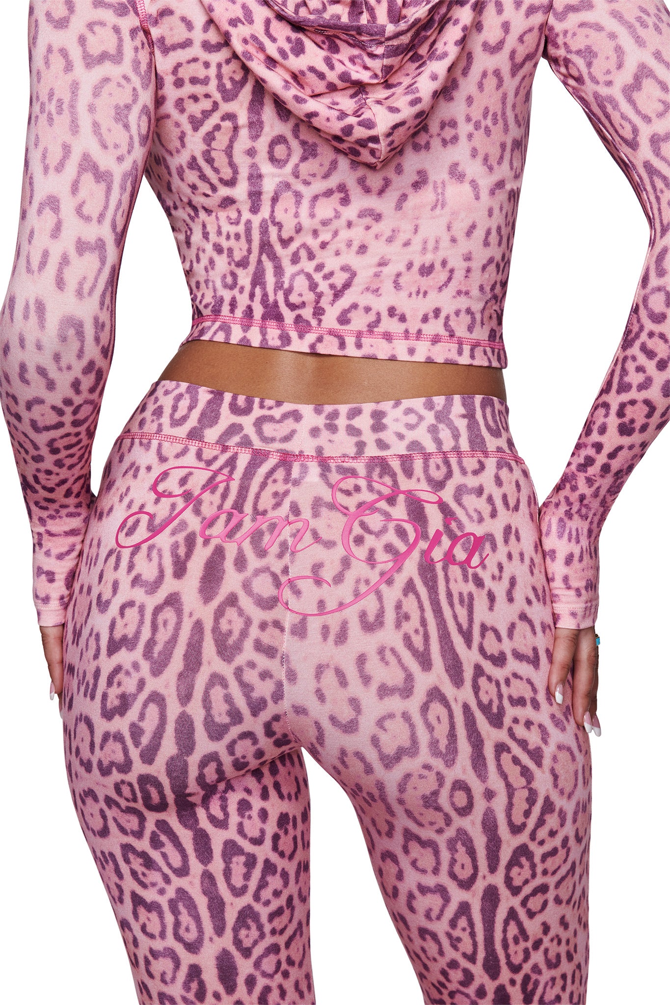 A person is shown from the back wearing I.AM.GIA’s BLARE TRACKPANT - PINK PANTHERA with flared legs and a matching leopard print hoodie; “I Am Gia” appears in pink script across the trackpant’s waistband.