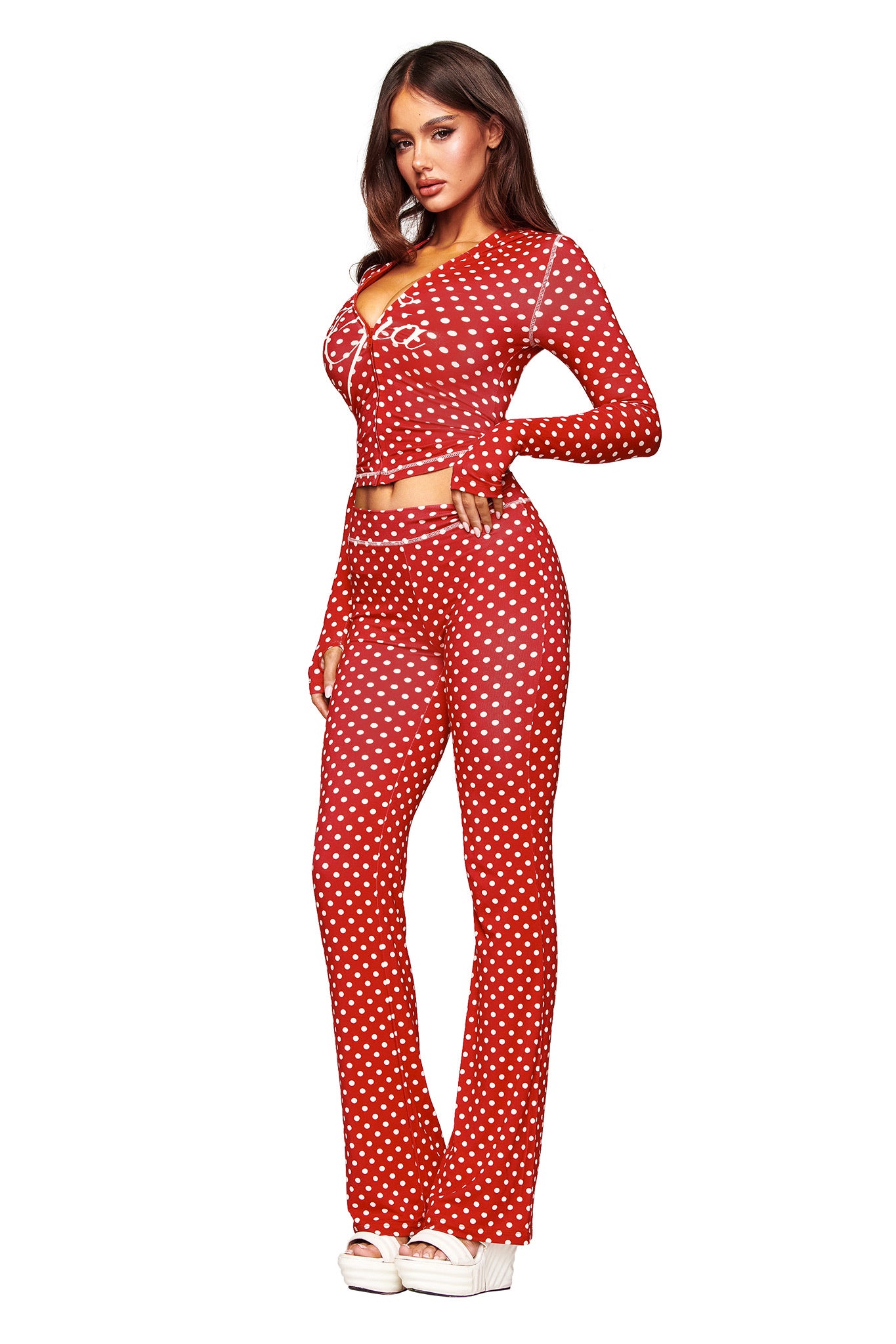 A woman models the I.AM.GIA BLARE TRACKPANT - RED POLKA DOT set with a matching long-sleeve fitted crop top and white platform shoes, against a white background.