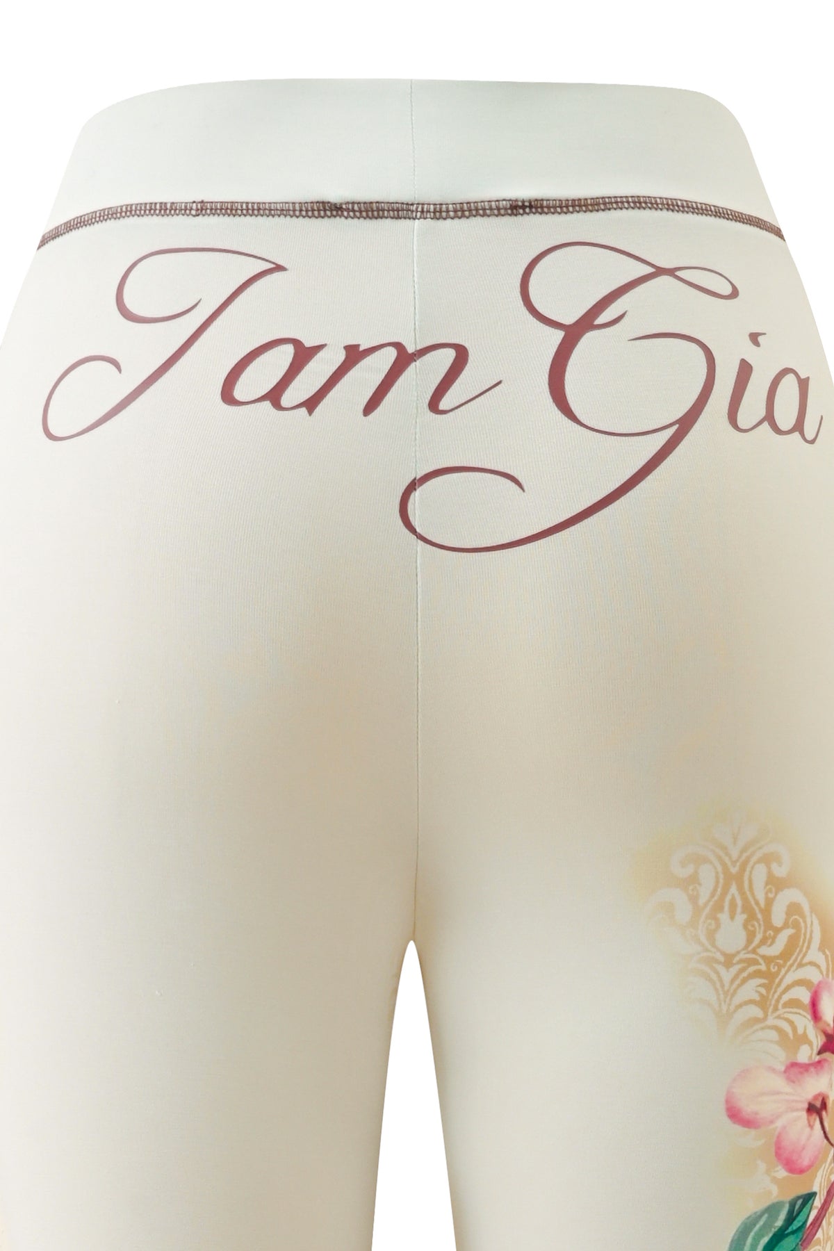 Close-up of the back of the cream-colored I.AM.GIA BLARE TRACKPANT – BLOSSOM, featuring “I am Gia” in pink cursive on the waistband and a partial floral print on the right leg.