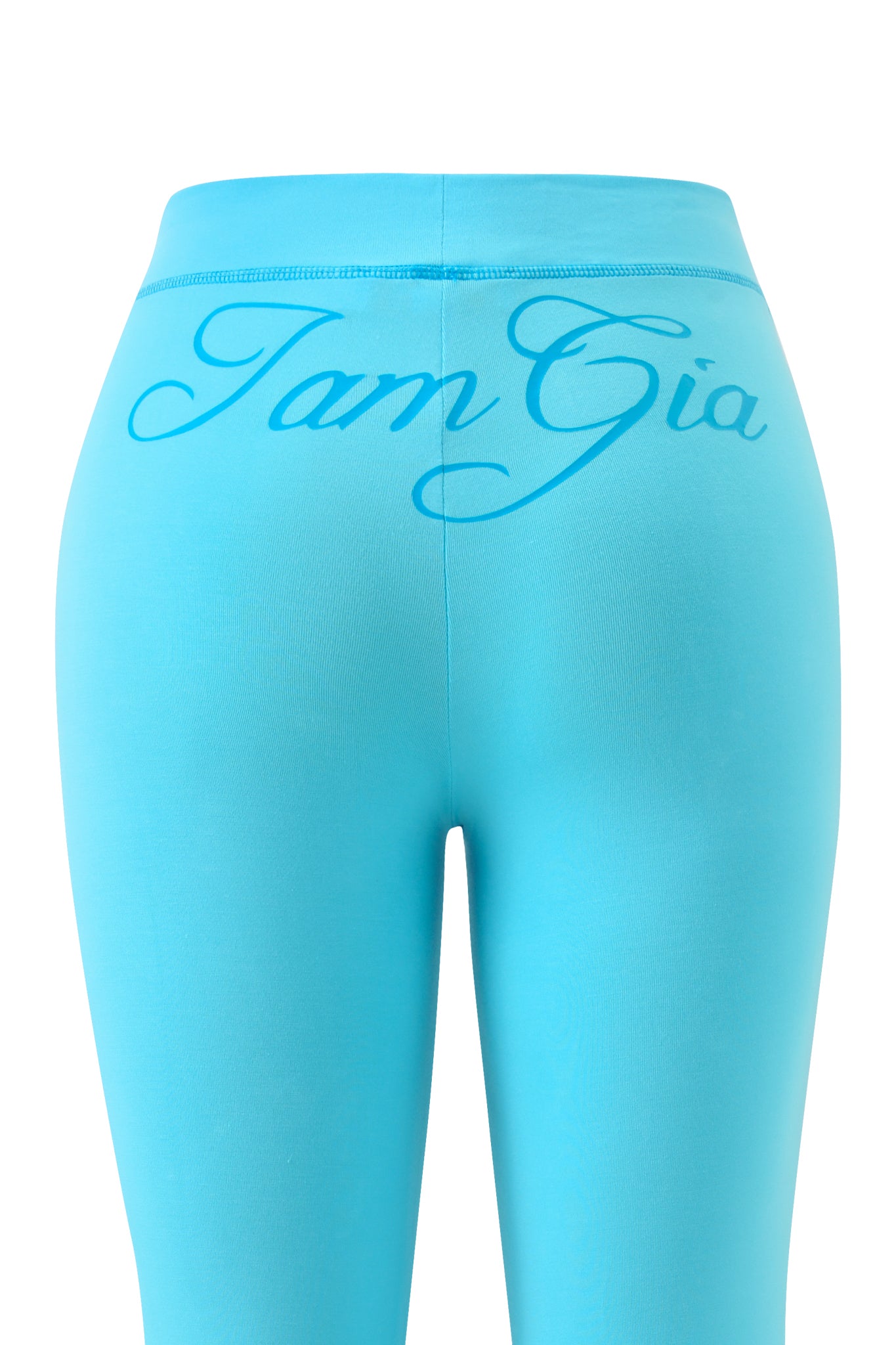 The BLARE TRACKPANT - NEON BLUE by I.AM.GIA features bold logo detailing across the waistband and upper back. The image highlights the vibrant flare design around the waist and hips, set against a crisp white backdrop.